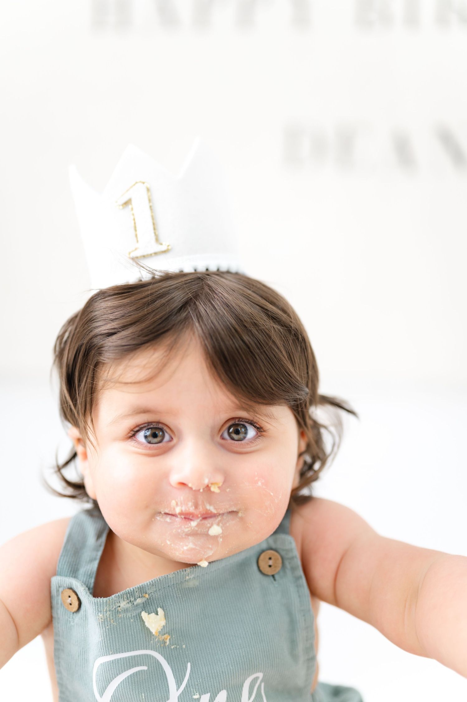 Cute baby wearing a number one birthday crown with cake on face, celebrating first birthday party.