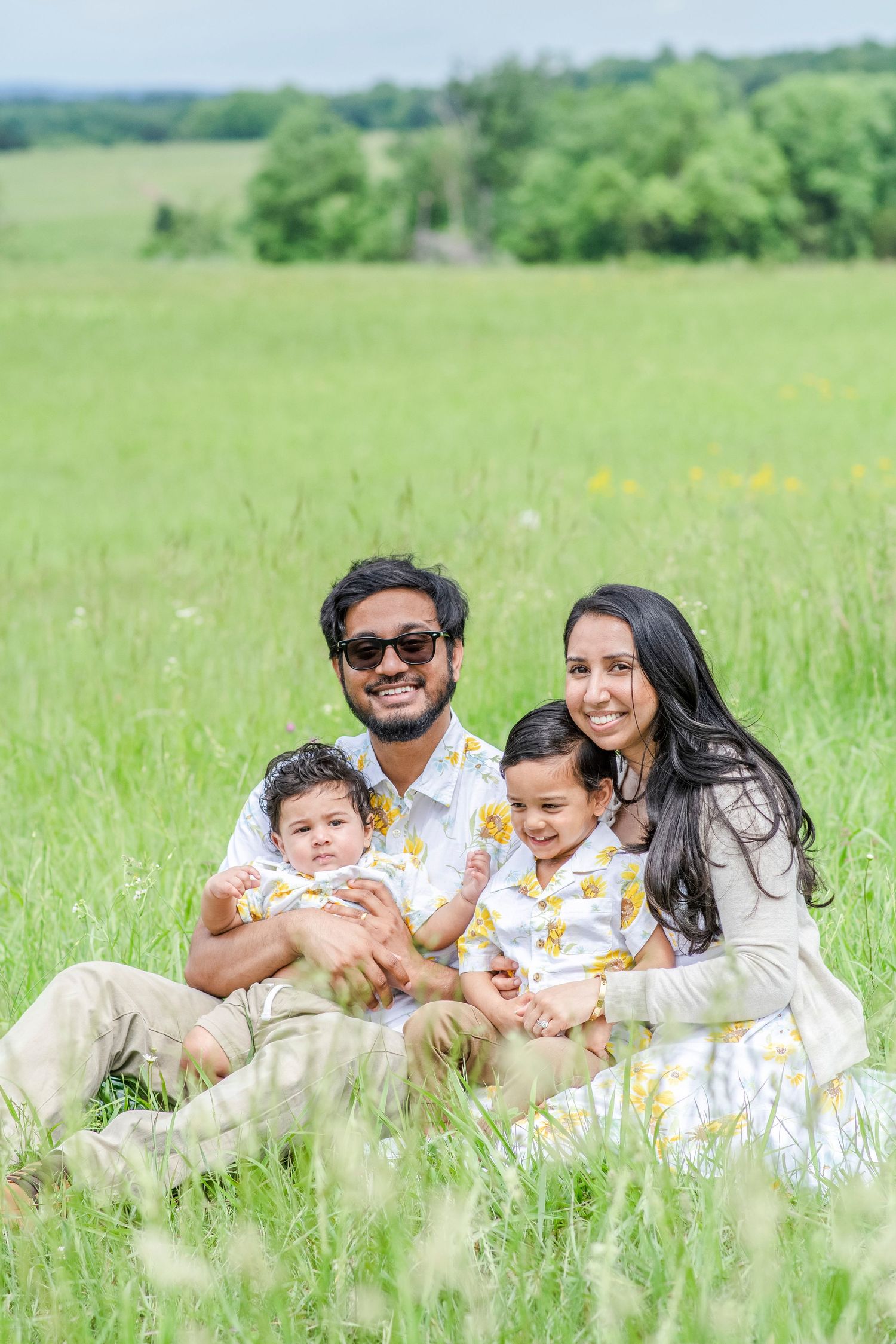 Family lying together in tall grass during a playful outdoor photoshoot.