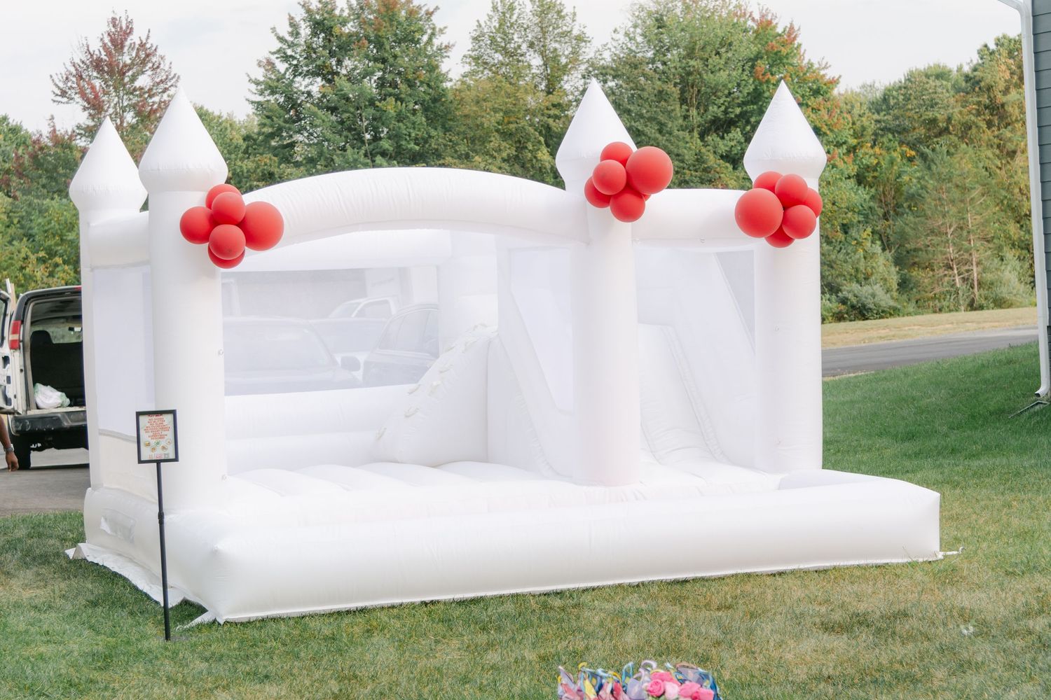 White inflatable bounce house with red balloon decorations set up on grass lawn for outdoor party entertainment.