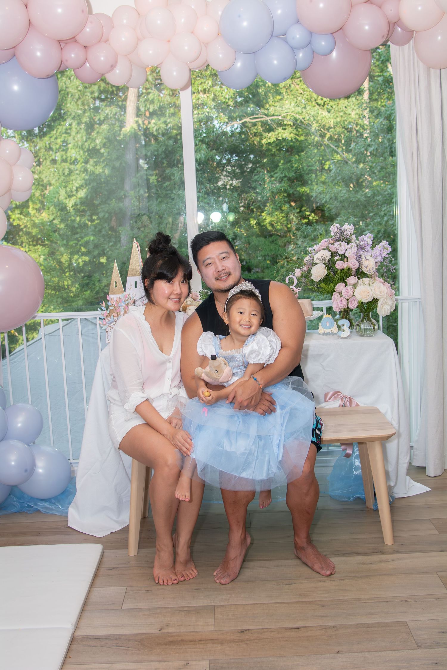 Family celebrates special occasion with pastel balloon decorations and tulle dress on wooden deck outdoors.