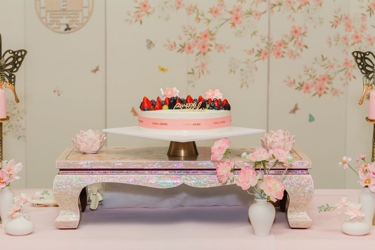 Cake display with butterfly decorations and pink floral accents on an ornate stand.