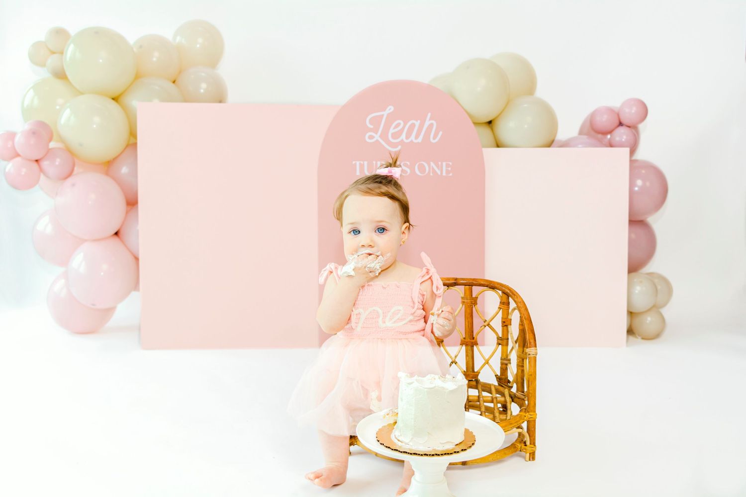 Elegant first birthday photo session setup with pastel balloons and wooden chair.