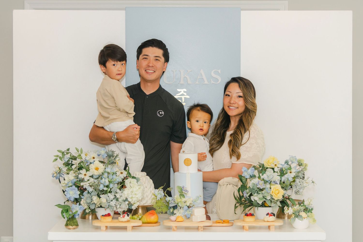 Family photo session against light blue backdrop with white floral decorations.