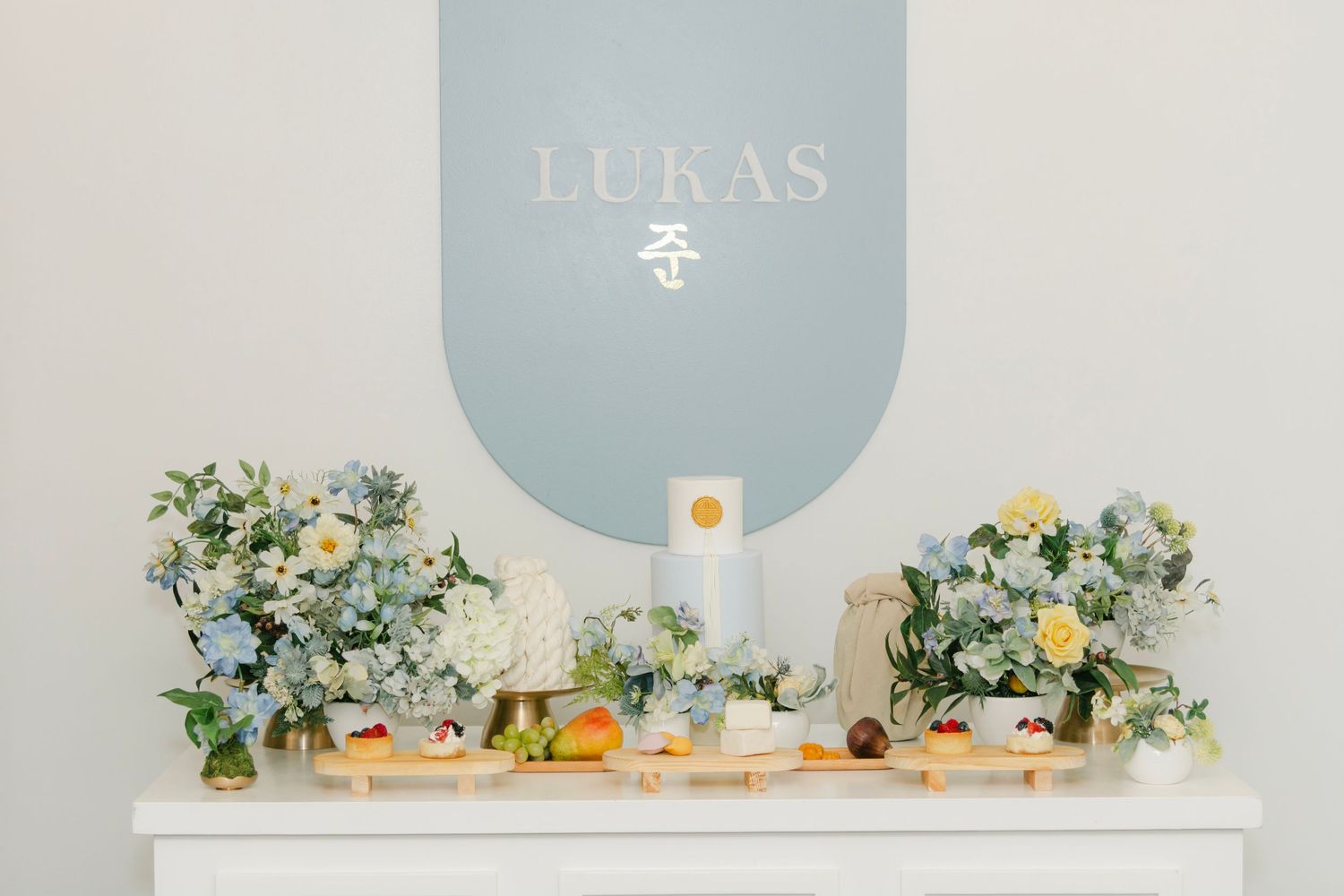 First birthday setup with white and blue decor featuring floral arrangements and toys on a white table.