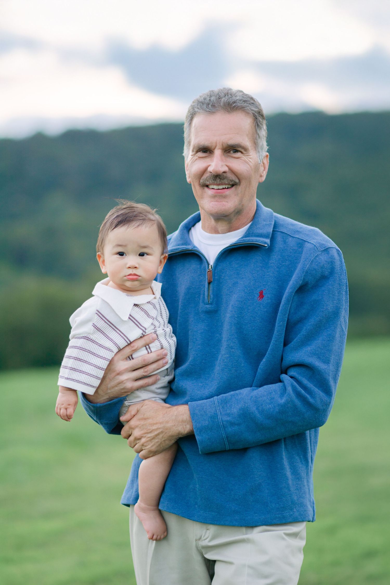 Sweet moment between family members in a blue sweater and striped outfit against green hills.
