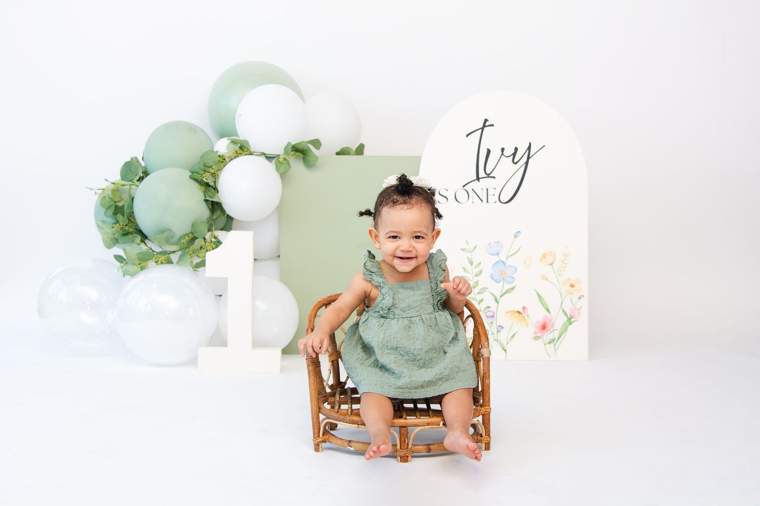 Cheerful baby in mint green outfit during milestone photo session with floral decorations.
