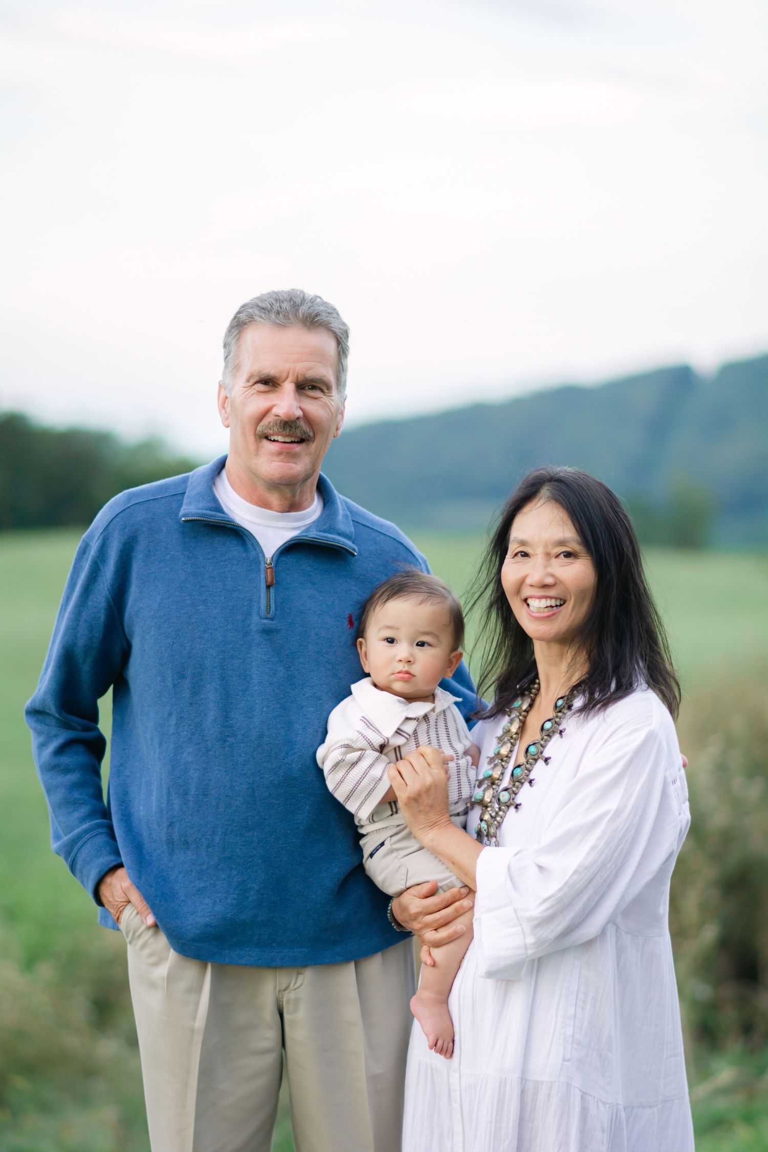 Family gathering on a hillside wearing coordinated white and blue outfits against a natural landscape.