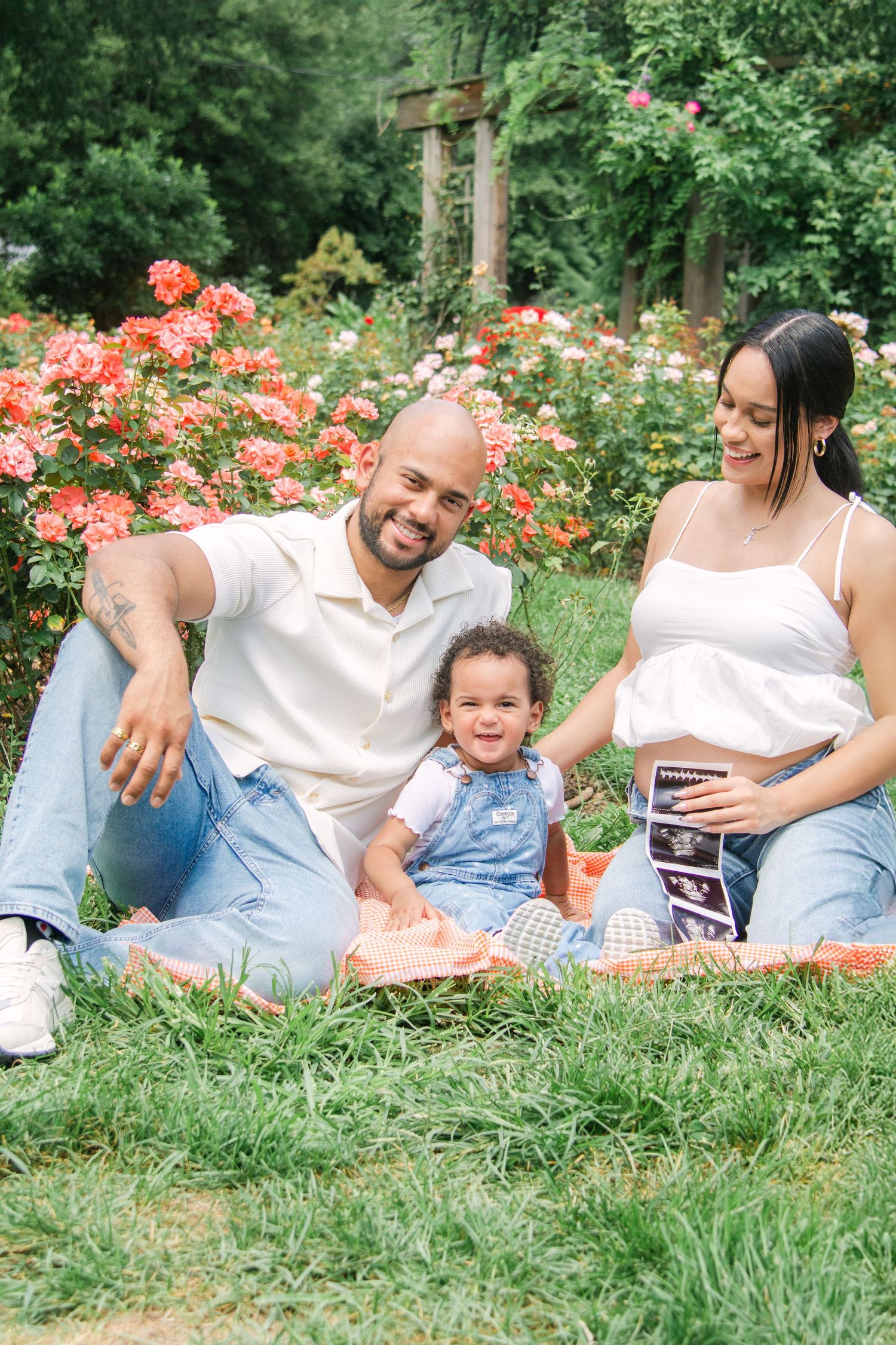 Happy family relaxing on blanket in flowering garden while looking at ultrasound images.