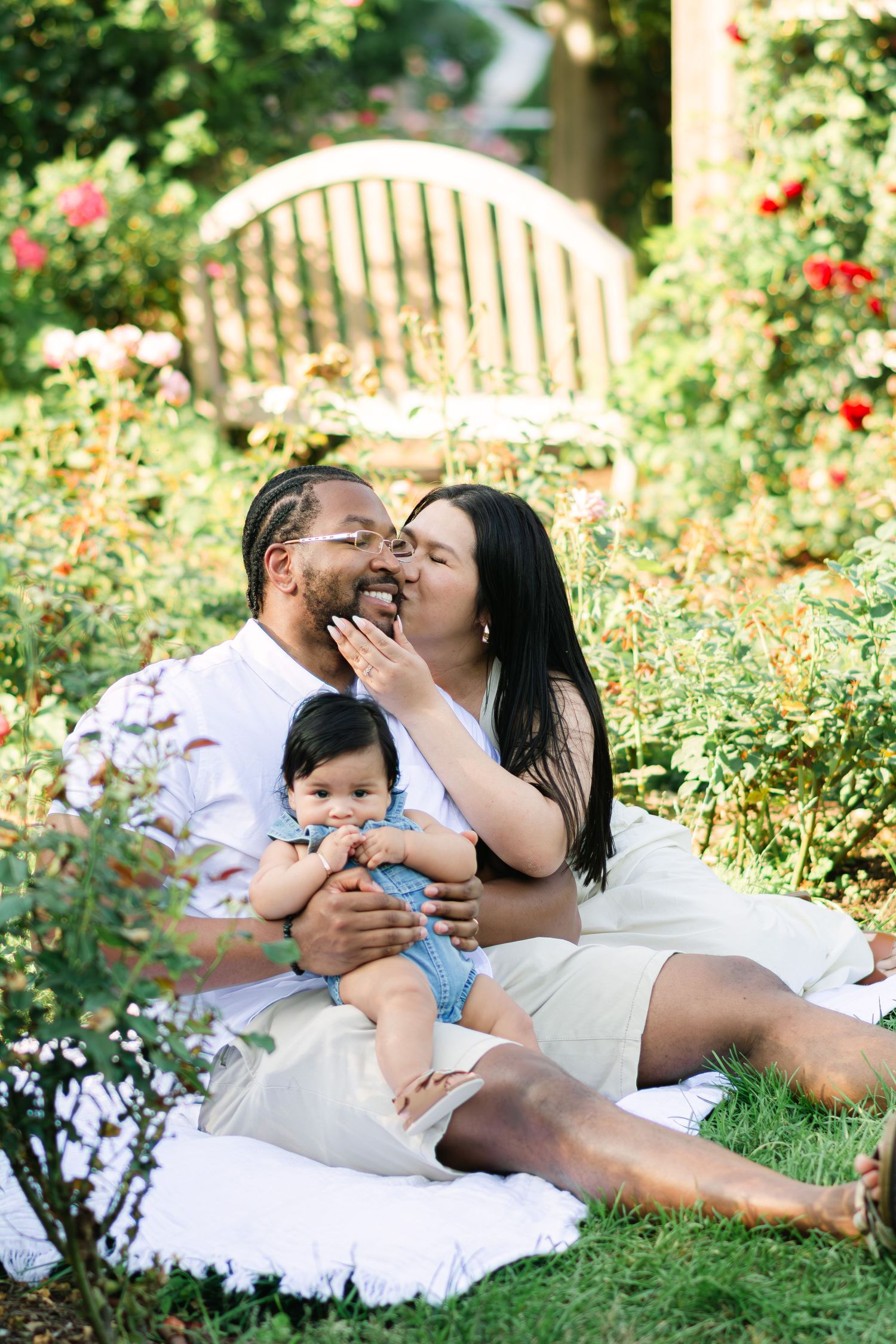 Family enjoying tender moment together on white blanket among blooming garden flowers.