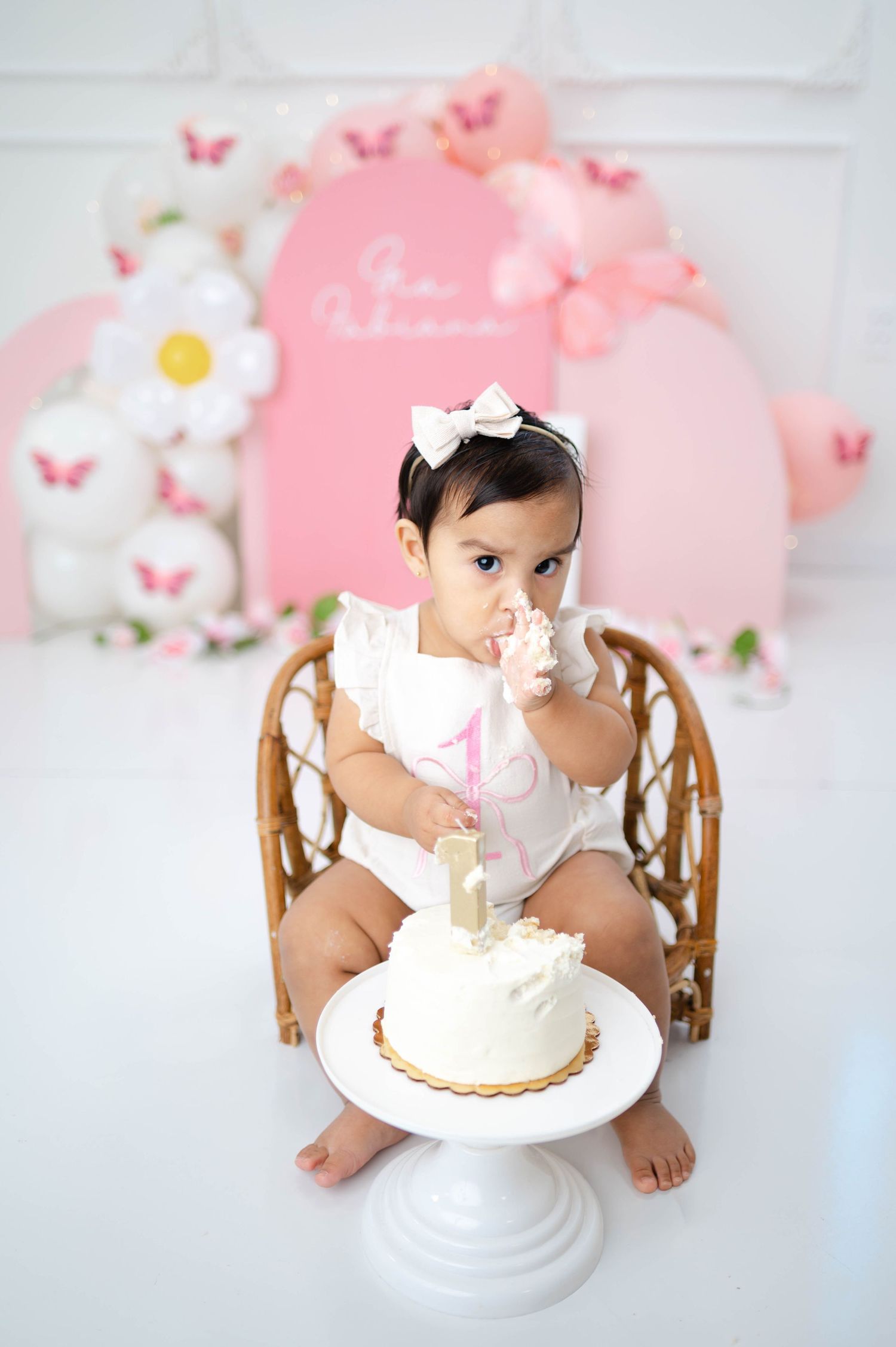 Cake smash photo session with pink butterflies and floral decorations on white background.