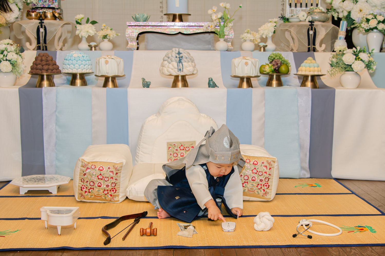Elegant baby photo setup with blue and white decorations, floral arrangements, and white seating areas.