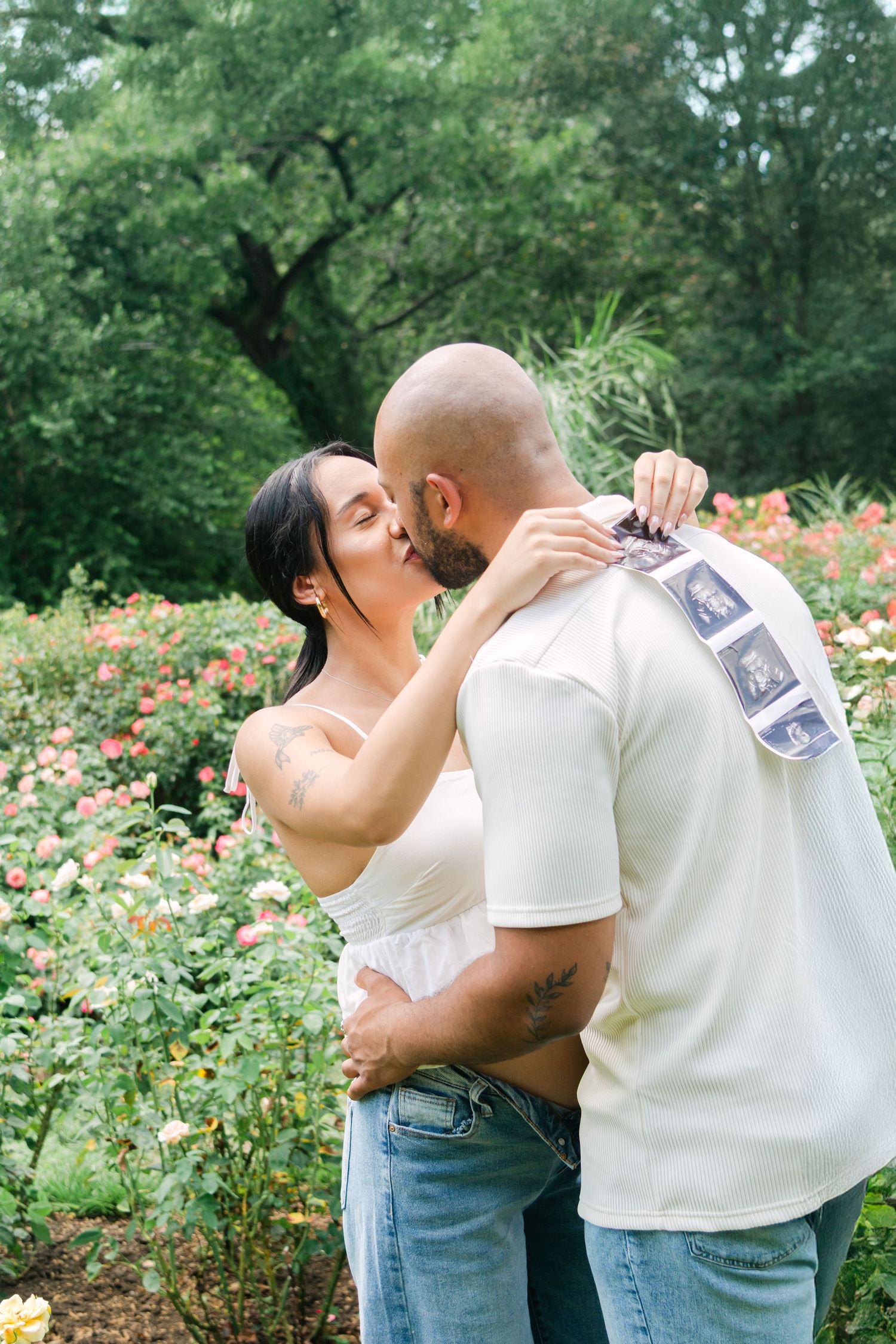 Intimate couple's photo session in a garden showing tender moments while holding sonogram pictures.