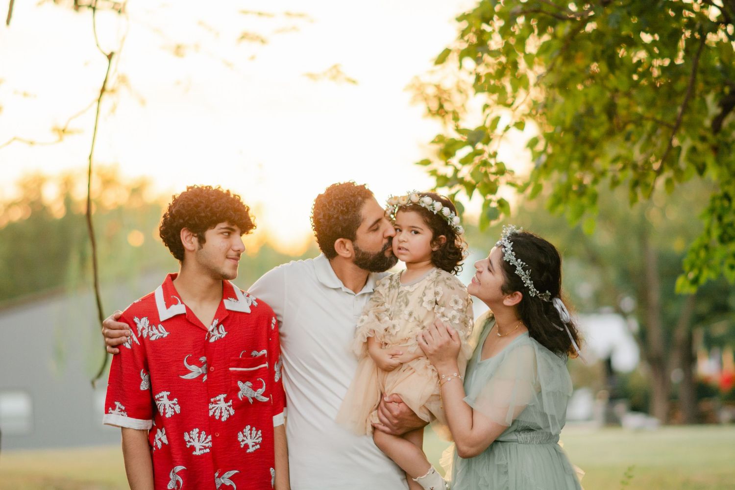 Family in matching red outfits share loving moments together in a sunny outdoor setting.