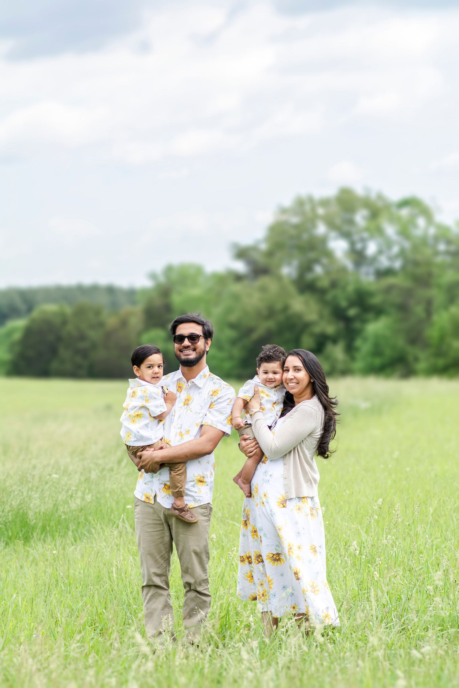 A family plays together in a sunny meadow wearing coordinated white and tan outfits.