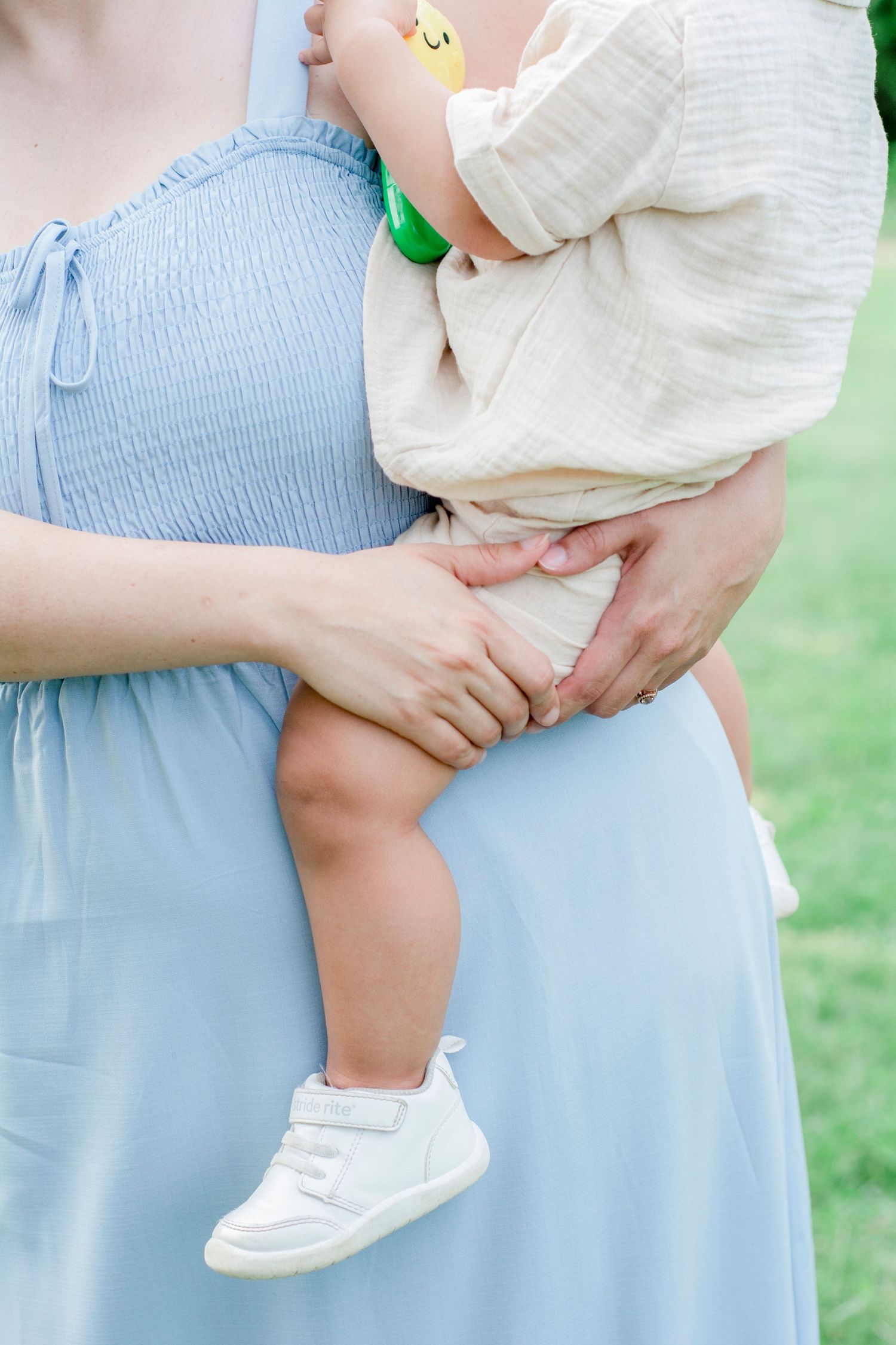 Close up of parent in blue dress holding baby's legs in white socks.