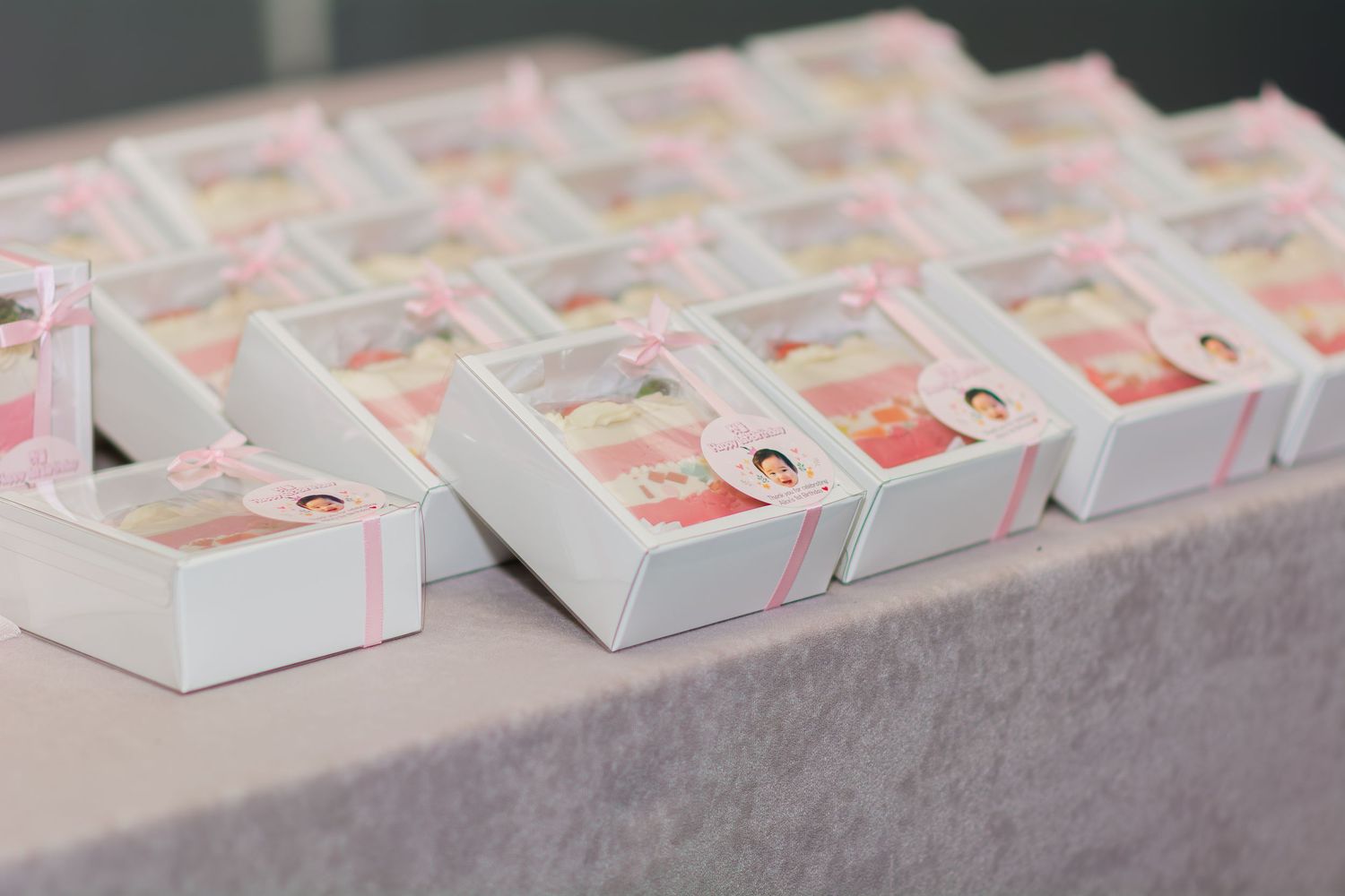Rows of white gift boxes with pink decorative details arranged on a table.