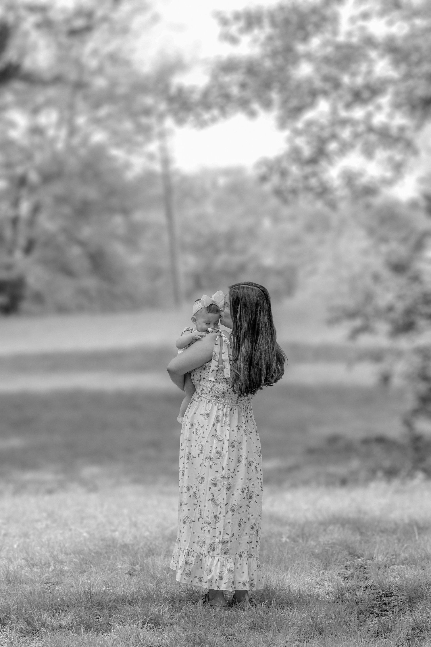 Dreamy monochrome image of figures in floral dresses standing in tall grass.