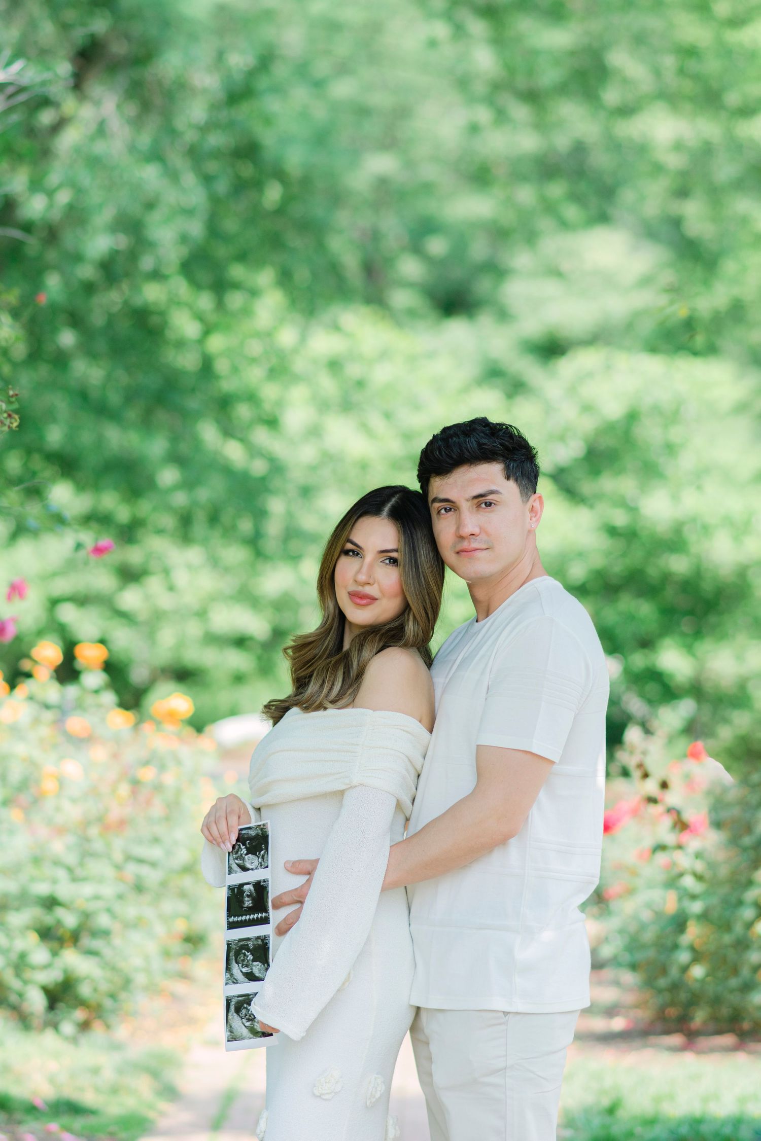 Outdoor pregnancy announcement photoshoot in garden with couple holding ultrasound photo.