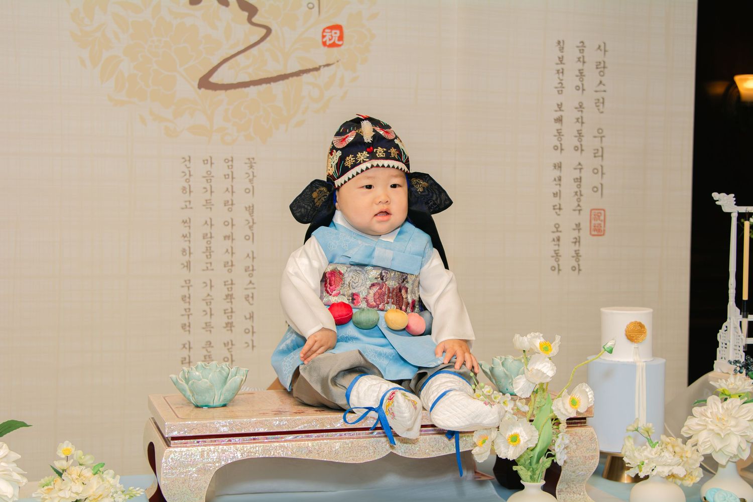 Korean dol celebration table with blue and white decor, featuring traditional items and floral arrangements.