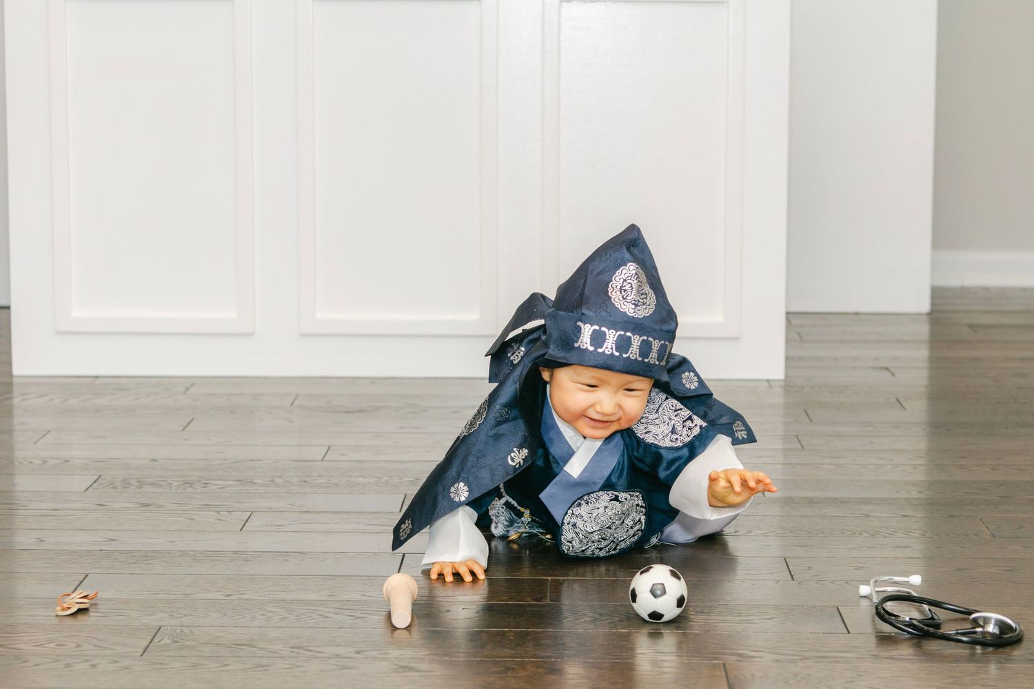 Small child in blue clothing lying on hardwood floor near toys and party decor.
