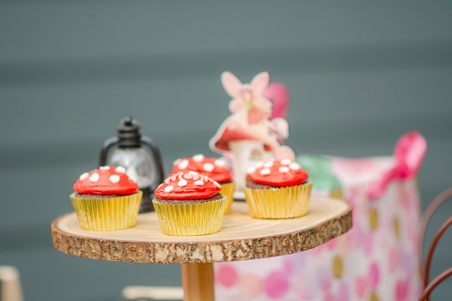 Pink frosted cupcakes arranged on a rustic wooden serving board with decorative sprinkles and garnishes.