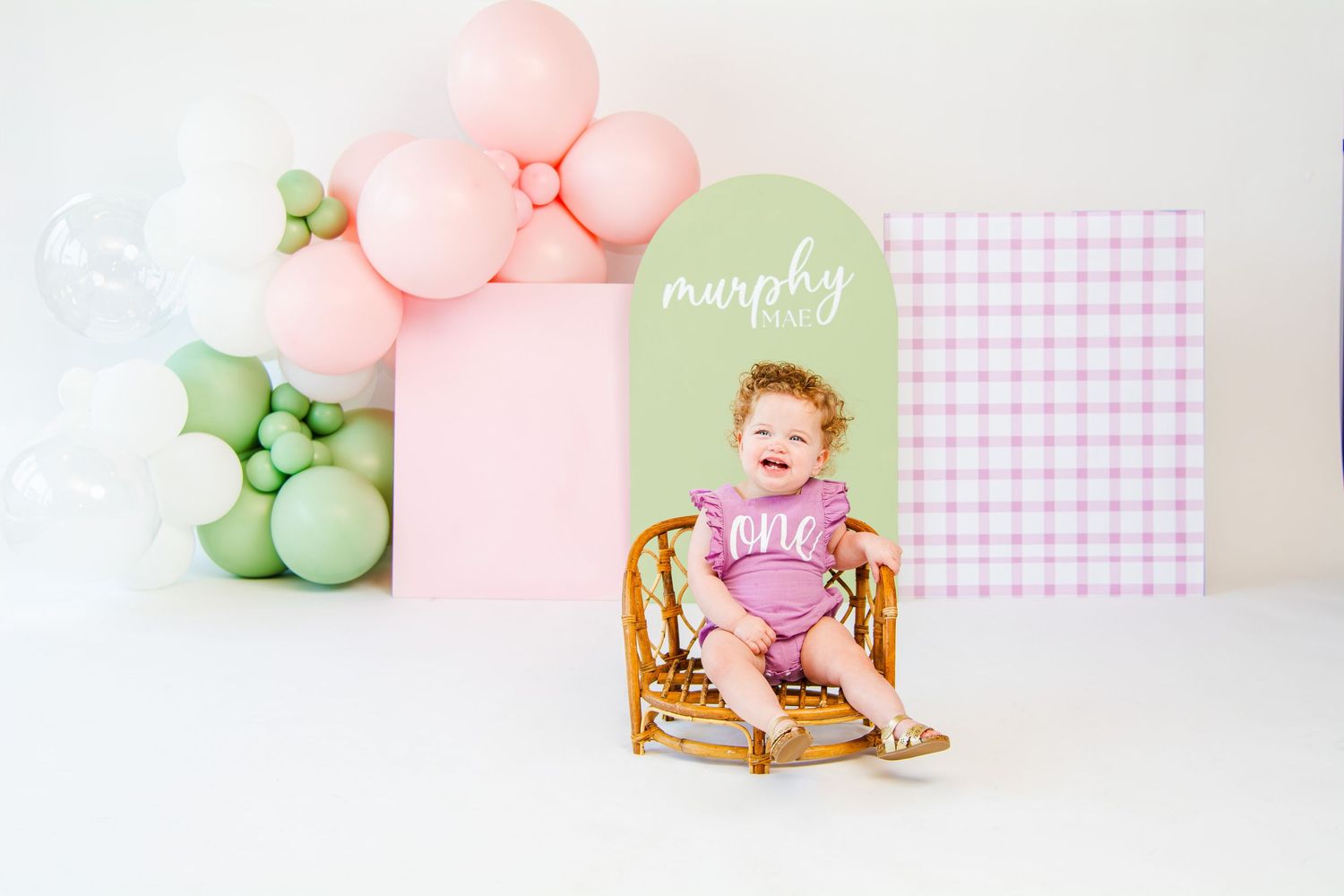 Birthday photo session with pink and green balloons and gingham pattern backdrop.