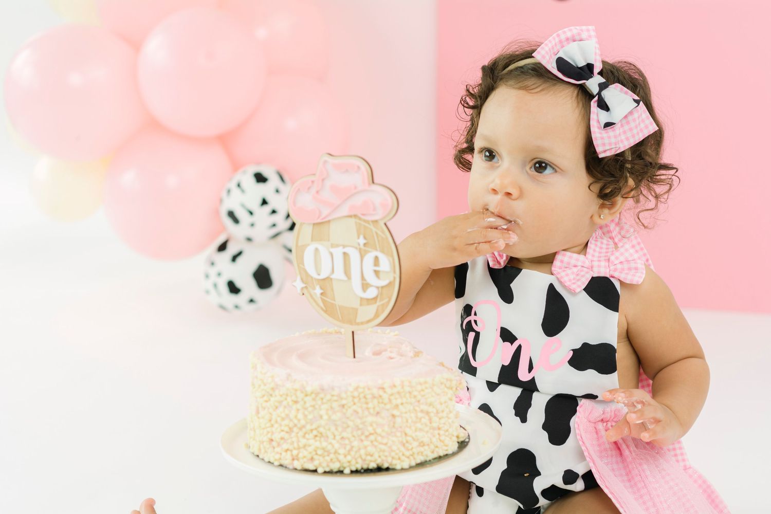 First birthday celebration with cow-print theme and pink balloons.