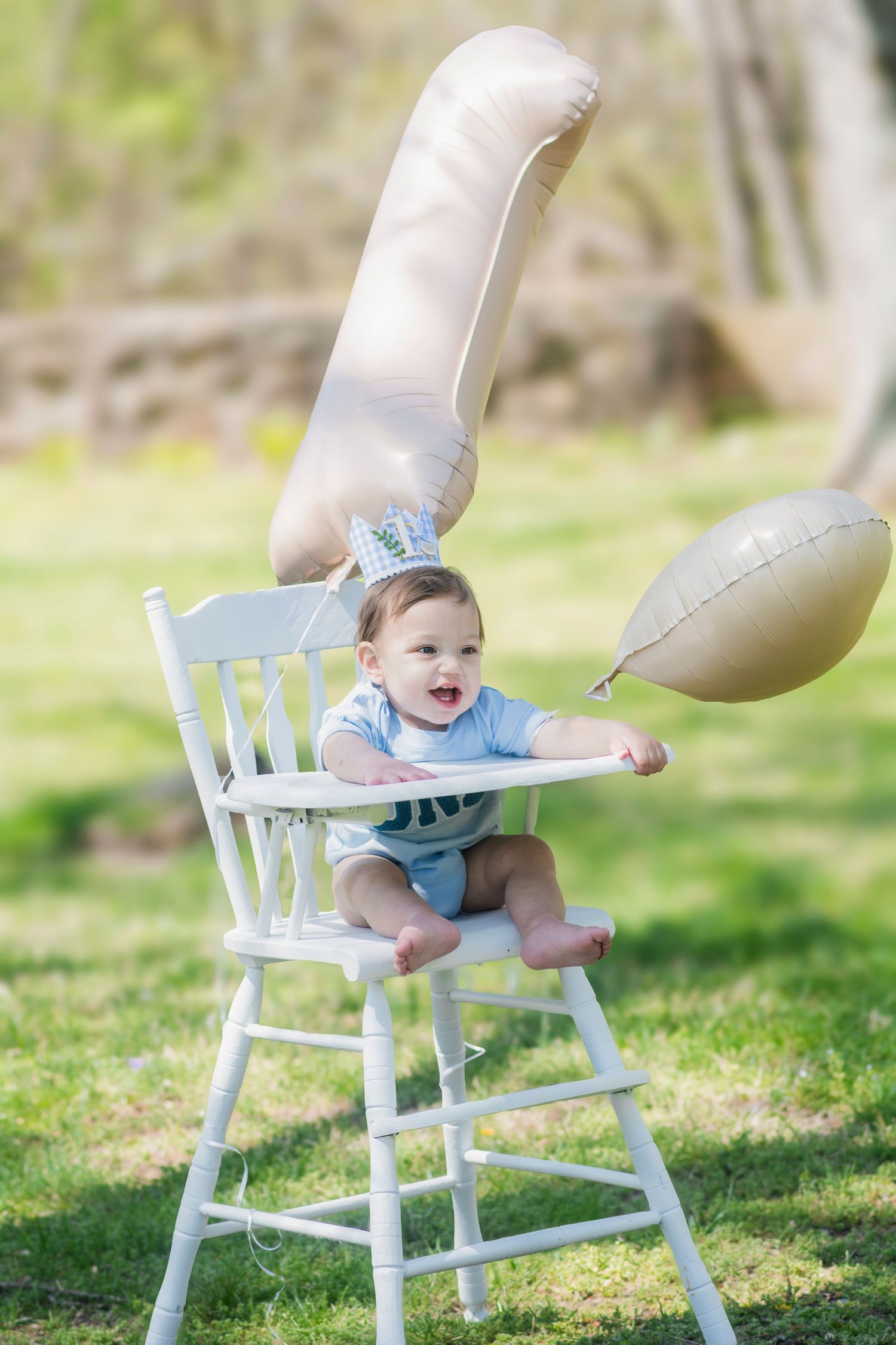 Baby in light blue outfit sits in a white vintage high chair on grassy outdoor setting.