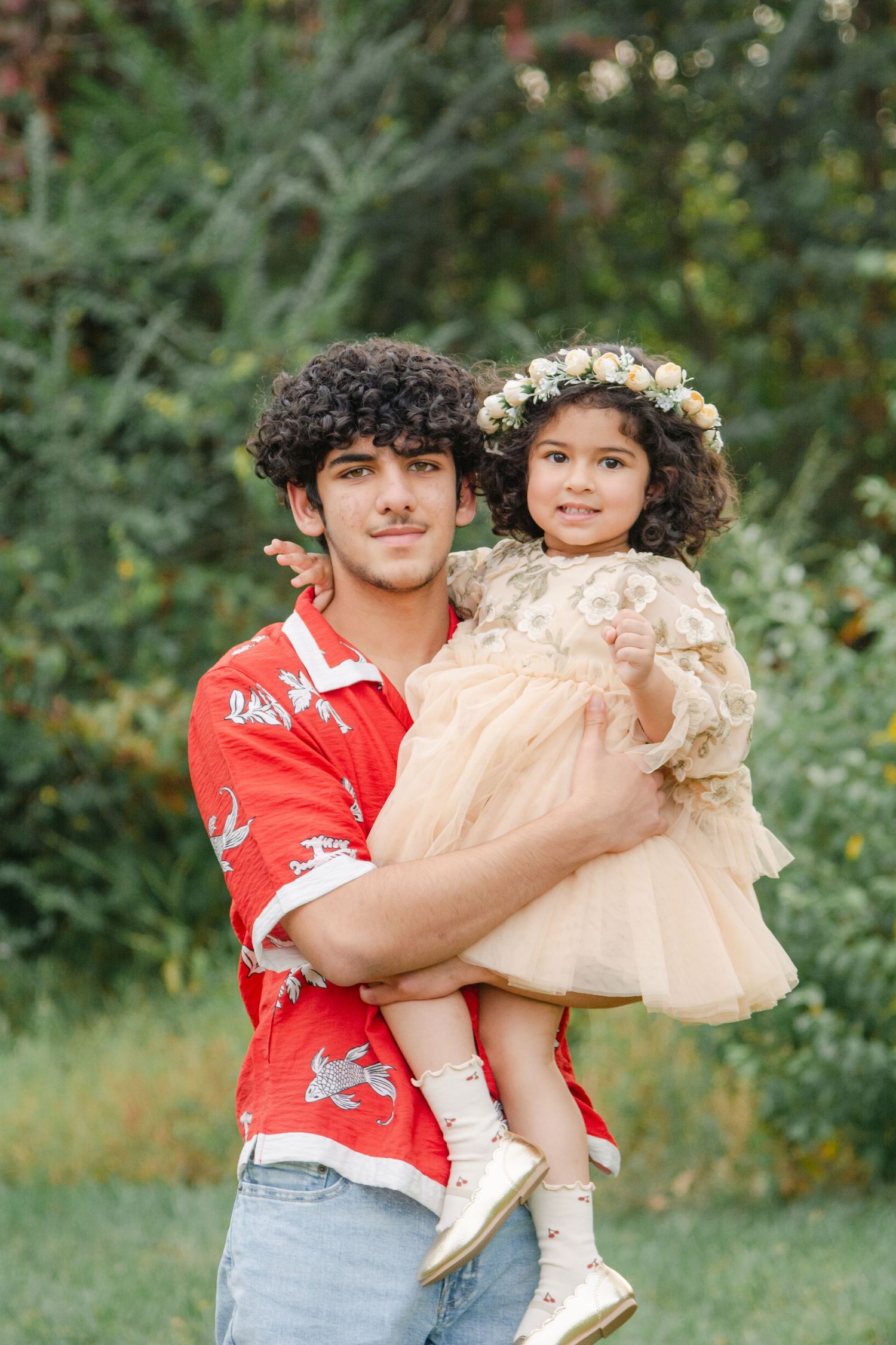 A pair in coordinated outfits pose together in a garden setting with greenery in the background.