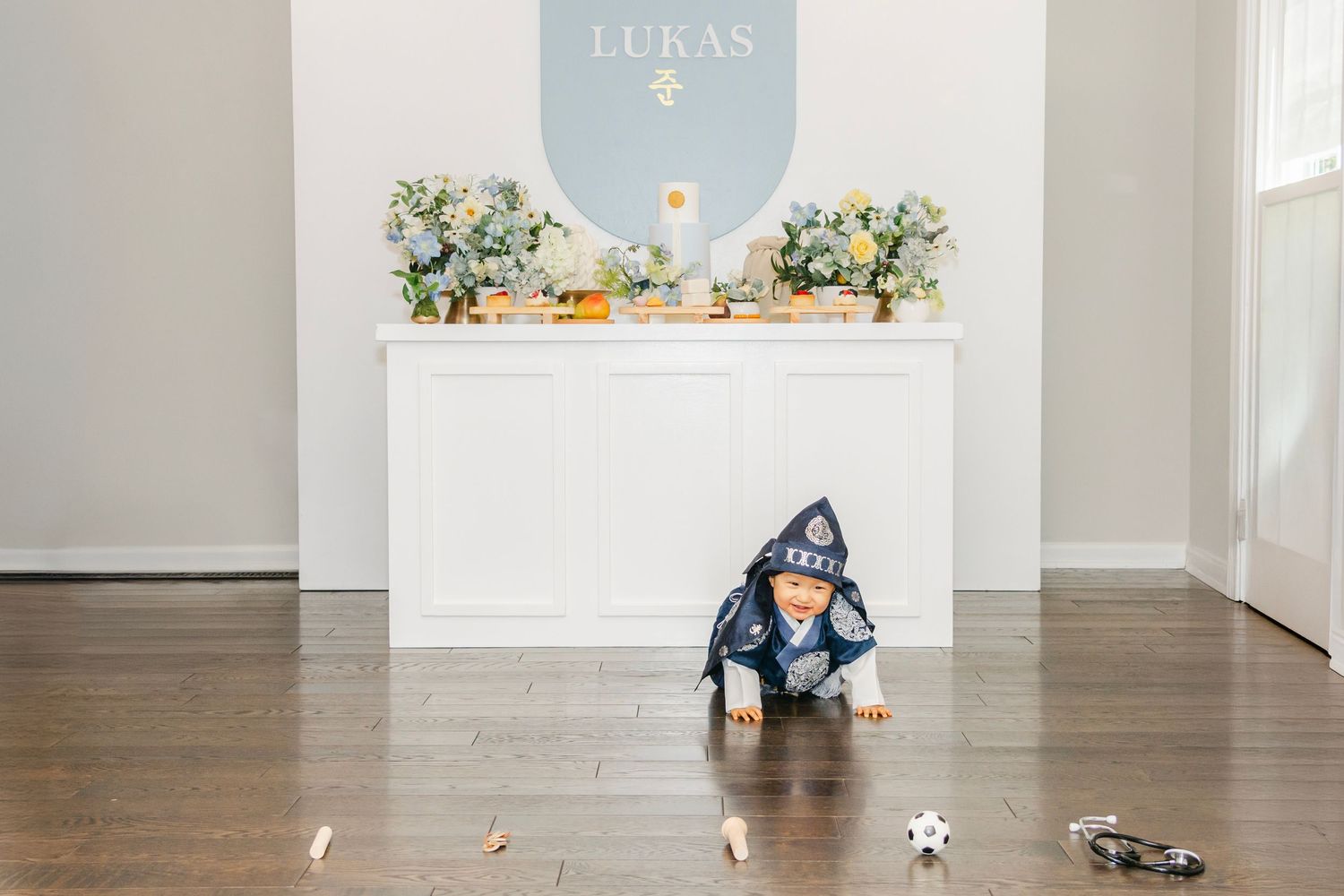 Birthday photo setup featuring white paneled walls and scattered toys on floor.