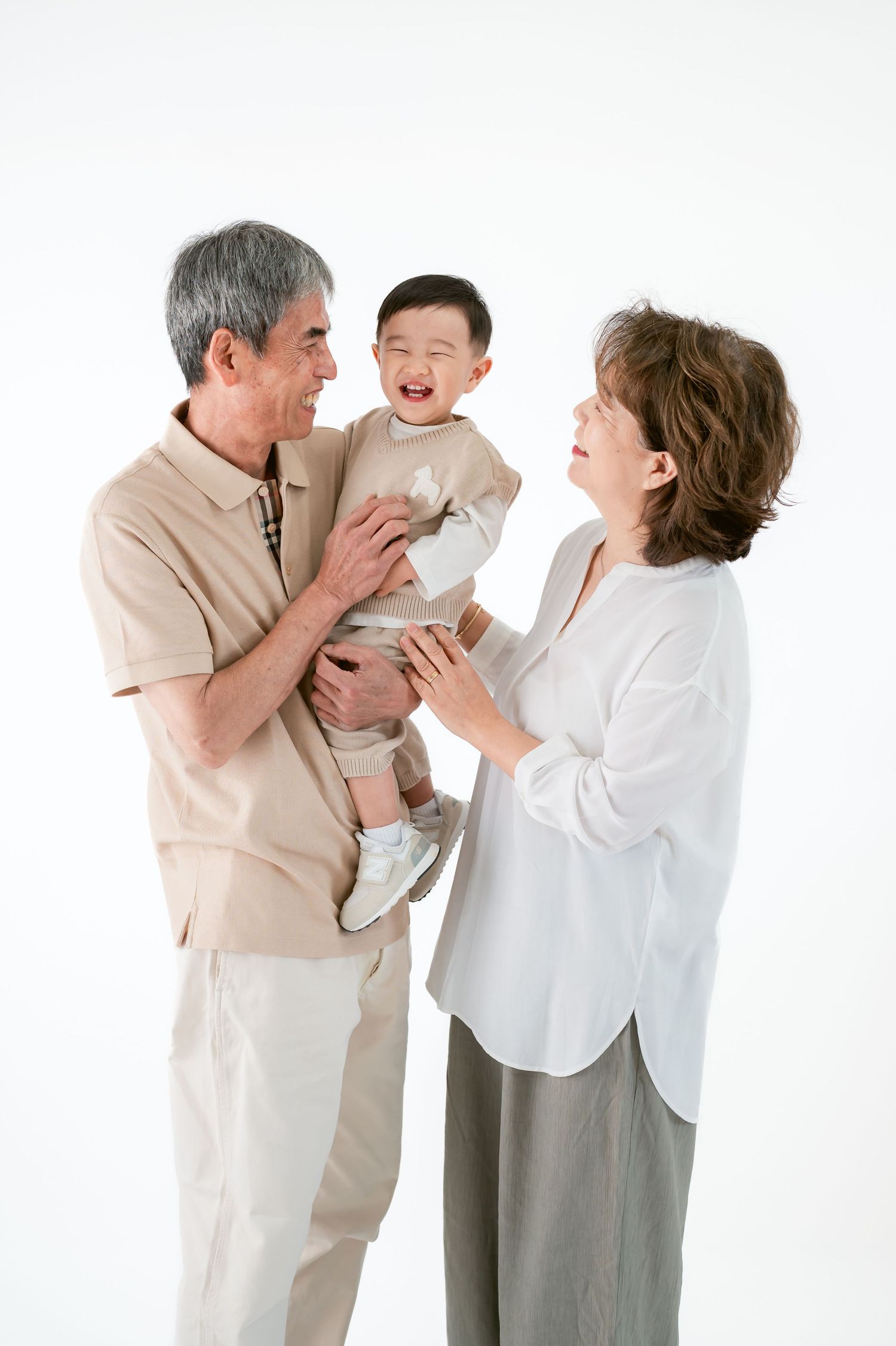 Grandparents smiling and holding a laughing baby together against a white background.