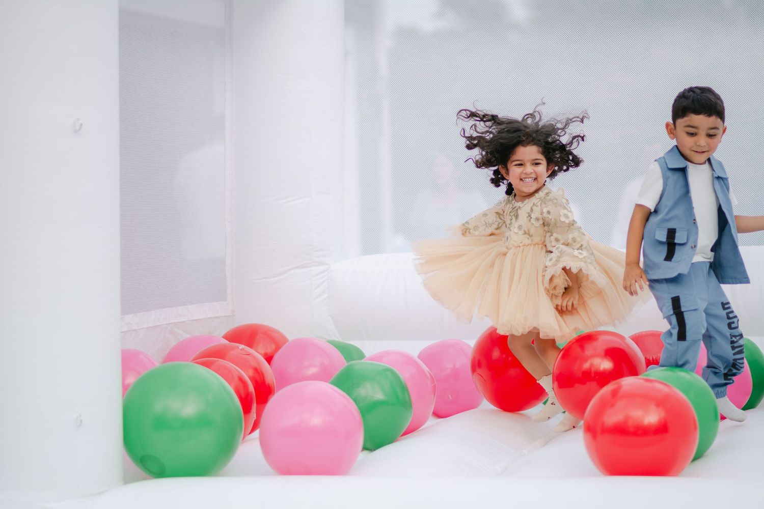 A group of children playing with colorful balloons in a bright indoor space.