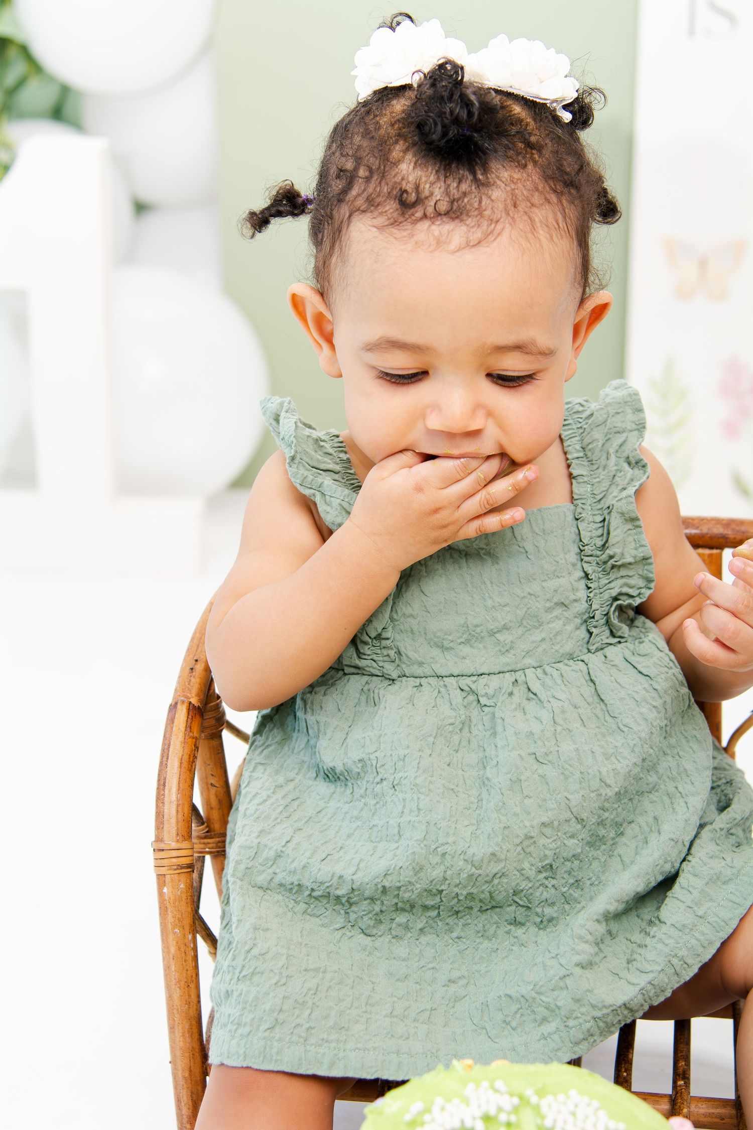 Baby in mint dress enjoying cake smash photo session with decorative backdrop.