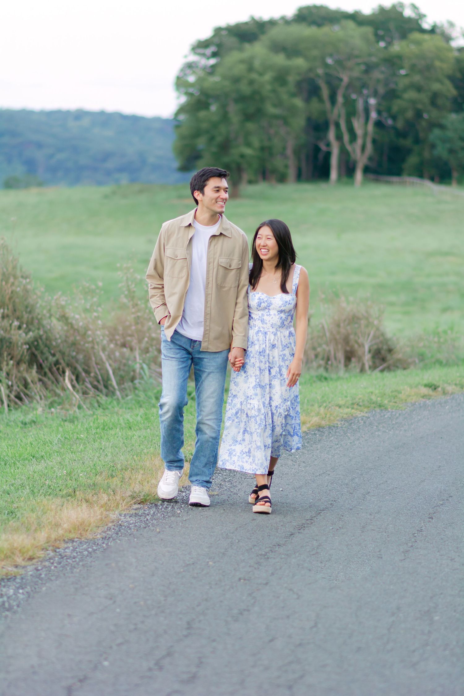 Couple walking together on a gravel path surrounded by green rolling hills and meadows.
