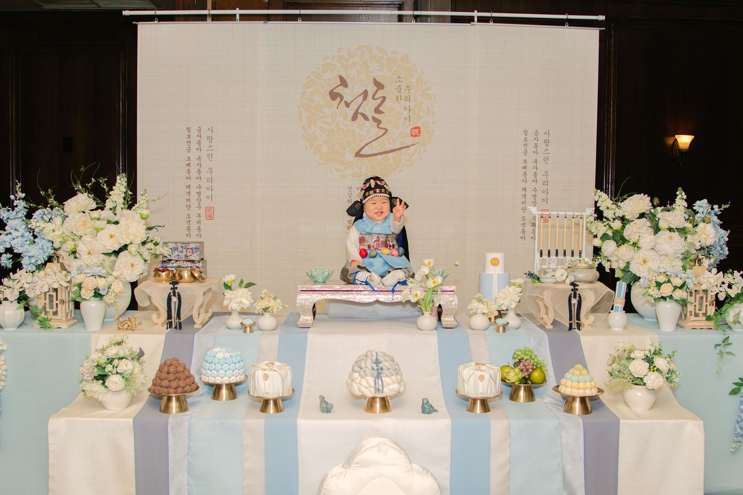 Long table decorated with Korean first birthday elements in soft blue and white color scheme.