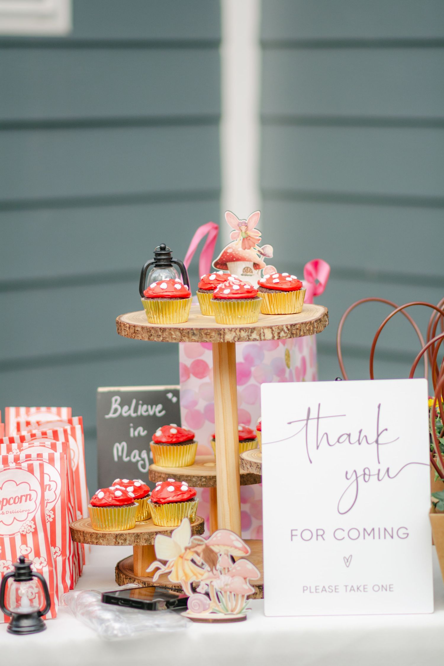 Pink and white cupcakes displayed on gold cake stands with thank you cards and party favors at a dessert table setup.