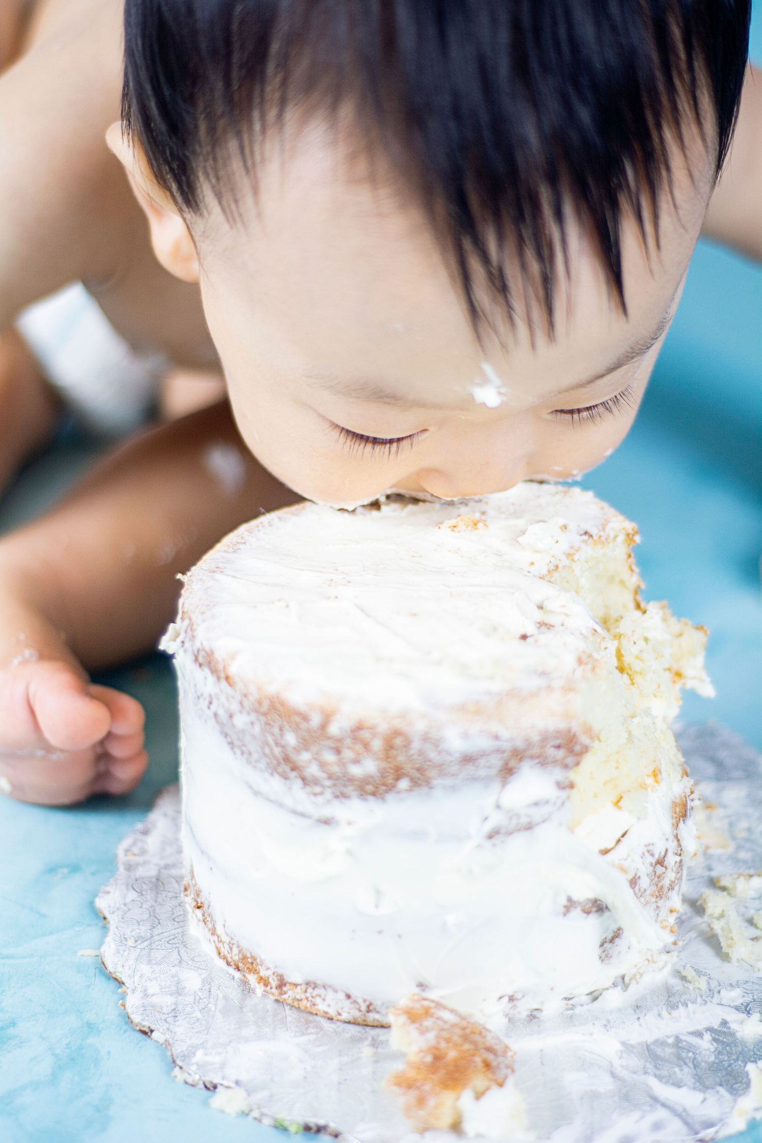 Close-up sequence of a baby eagerly eating white frosted cake and getting messy during a cake smash photoshoot.