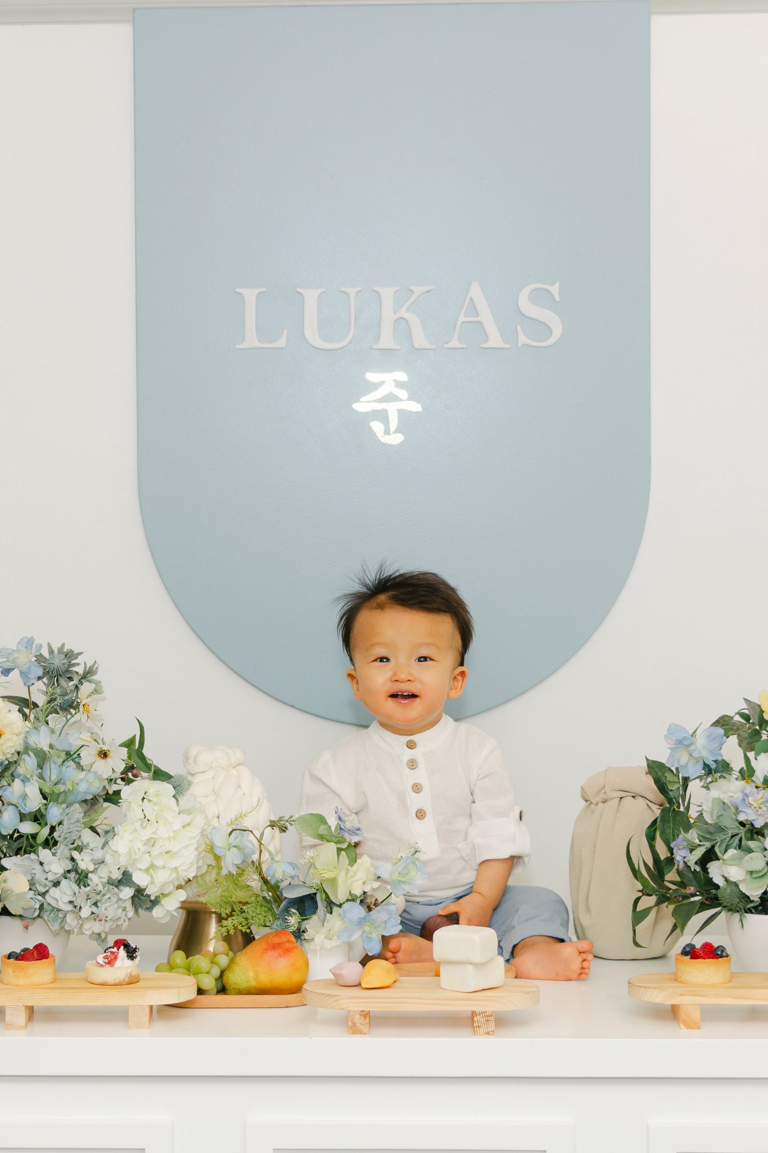 Baby's first birthday photoshoot with light blue backdrop and white floral decorations.