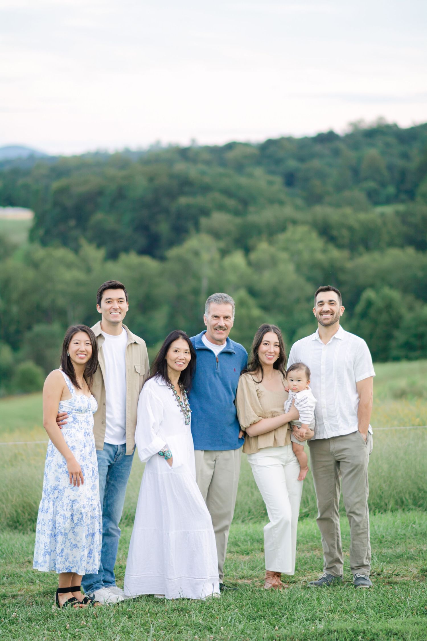 Extended family group photo in coordinated white and blue outfits against rolling green hills.