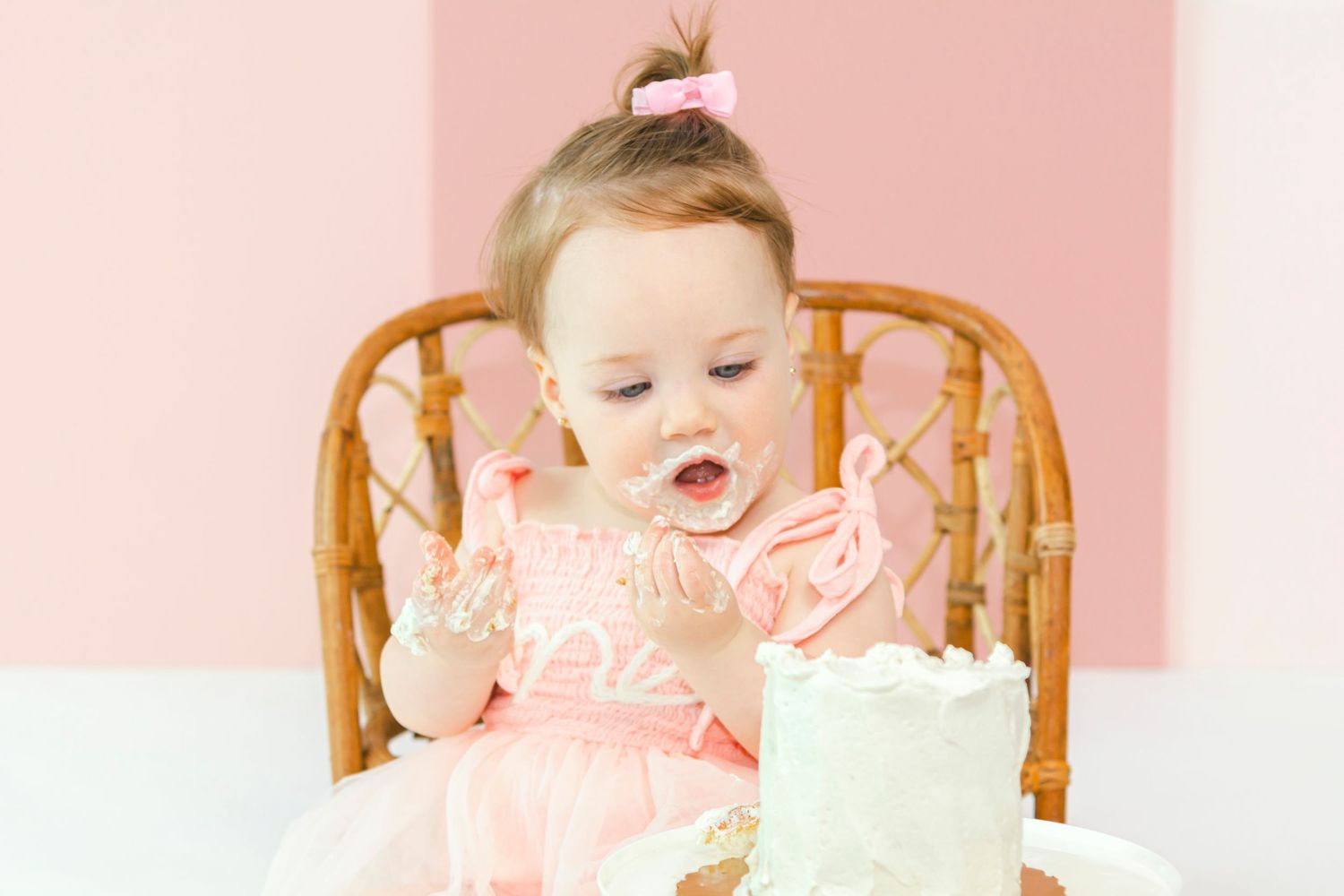 First birthday celebration setup with pink background and wooden high chair.