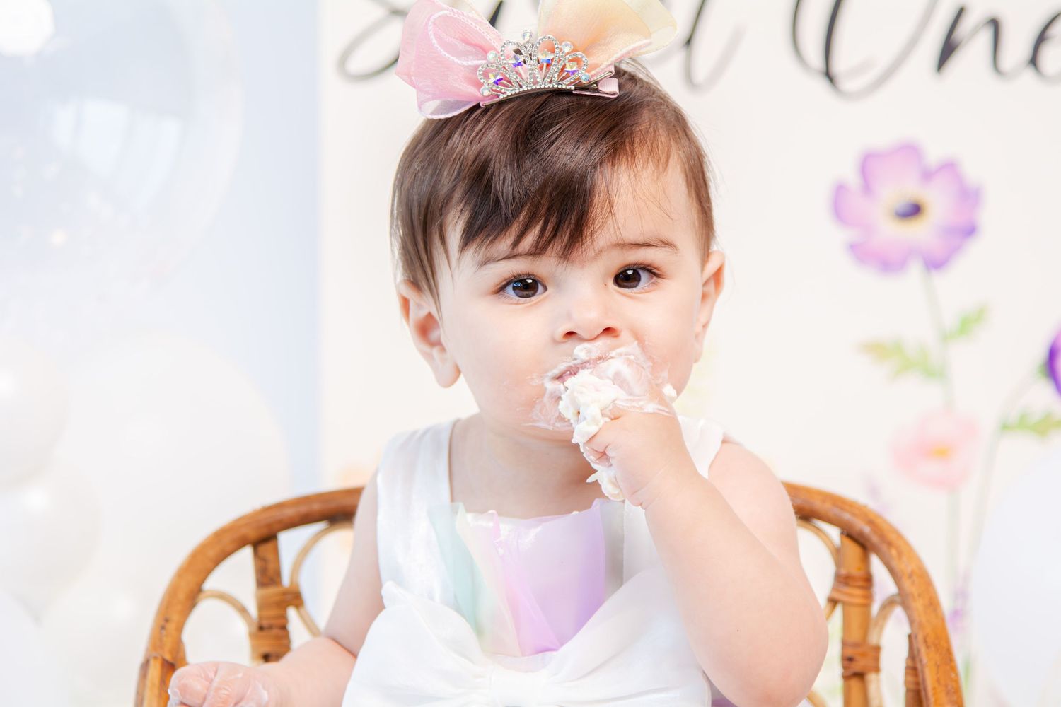 Close-up of baby enjoying cake smash session with pink and purple decorations.