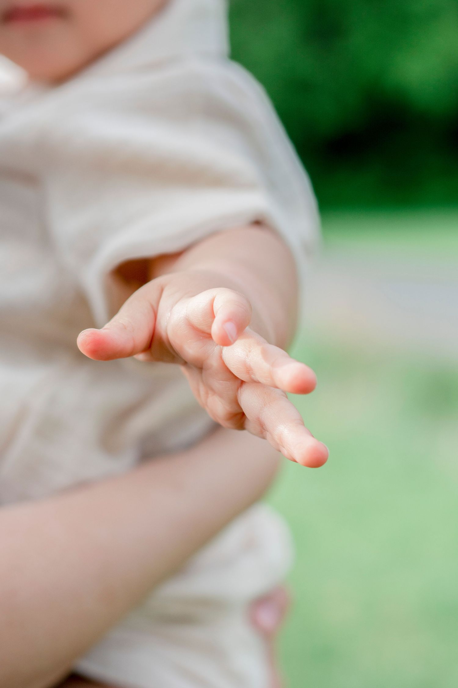 Close up of baby's delicate fingers reaching out against soft green background.