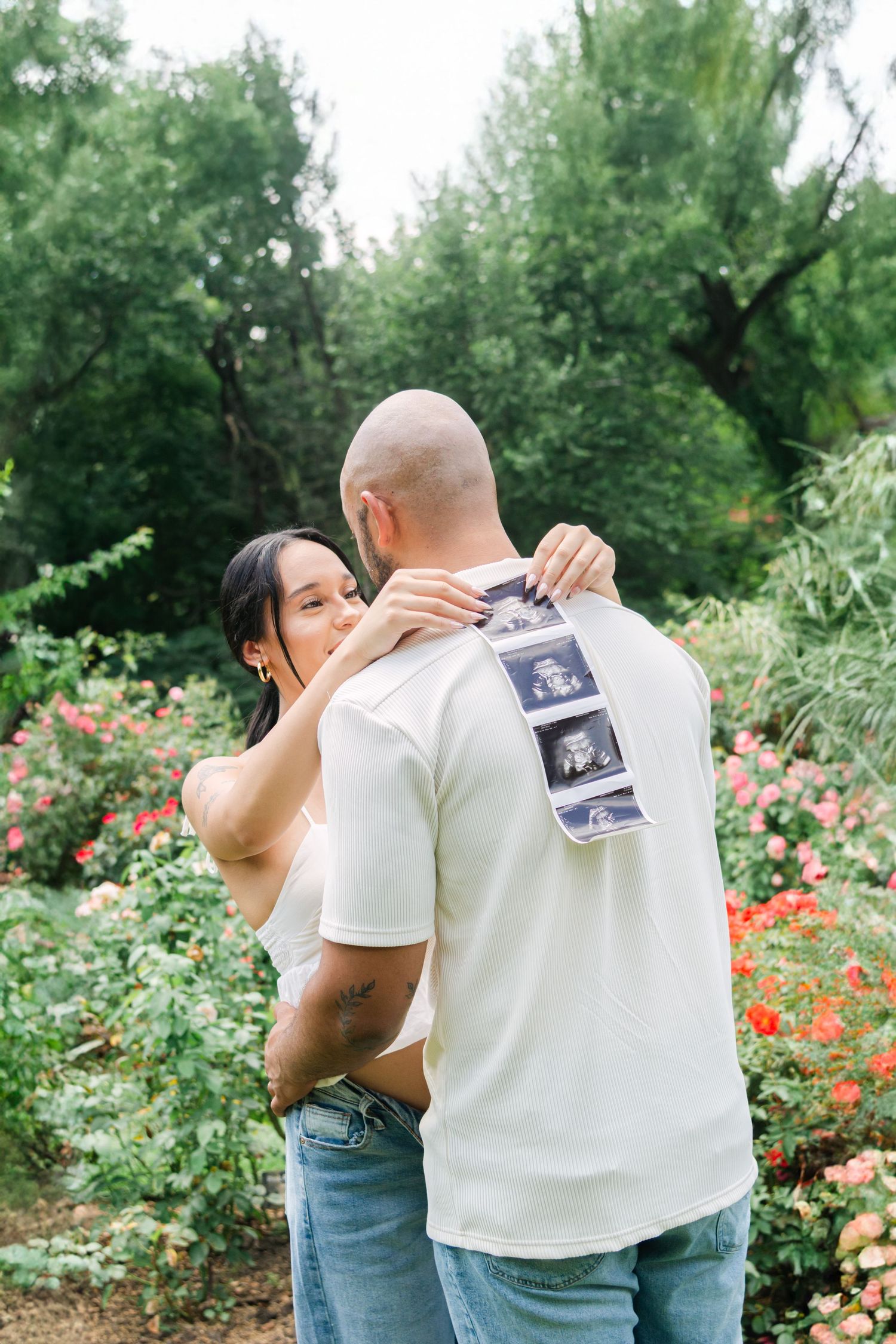 Tender family moment captured in a blooming rose garden while sharing pregnancy announcement photos.
