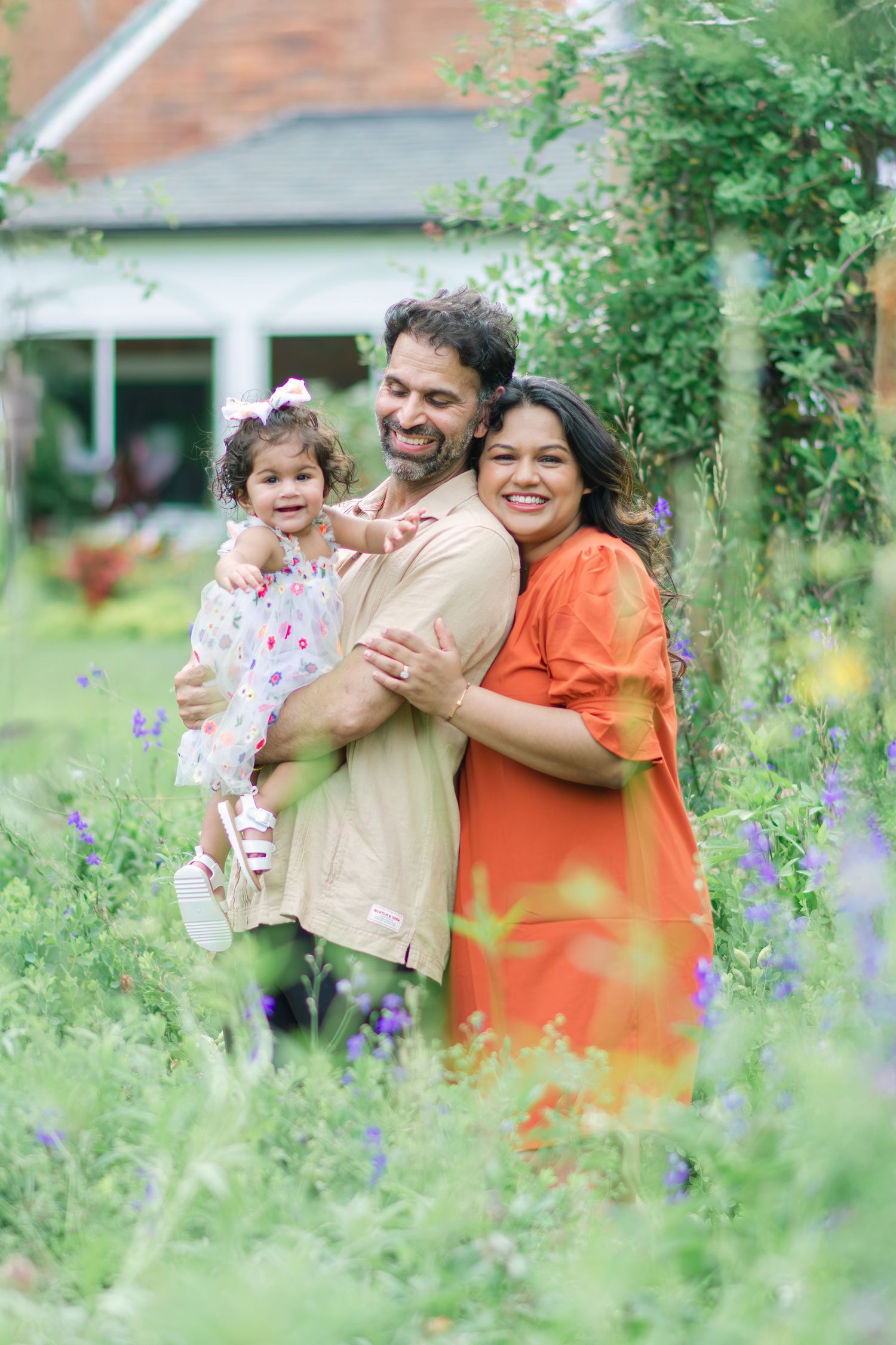 Family members embracing and laughing together in a garden with purple flowers.