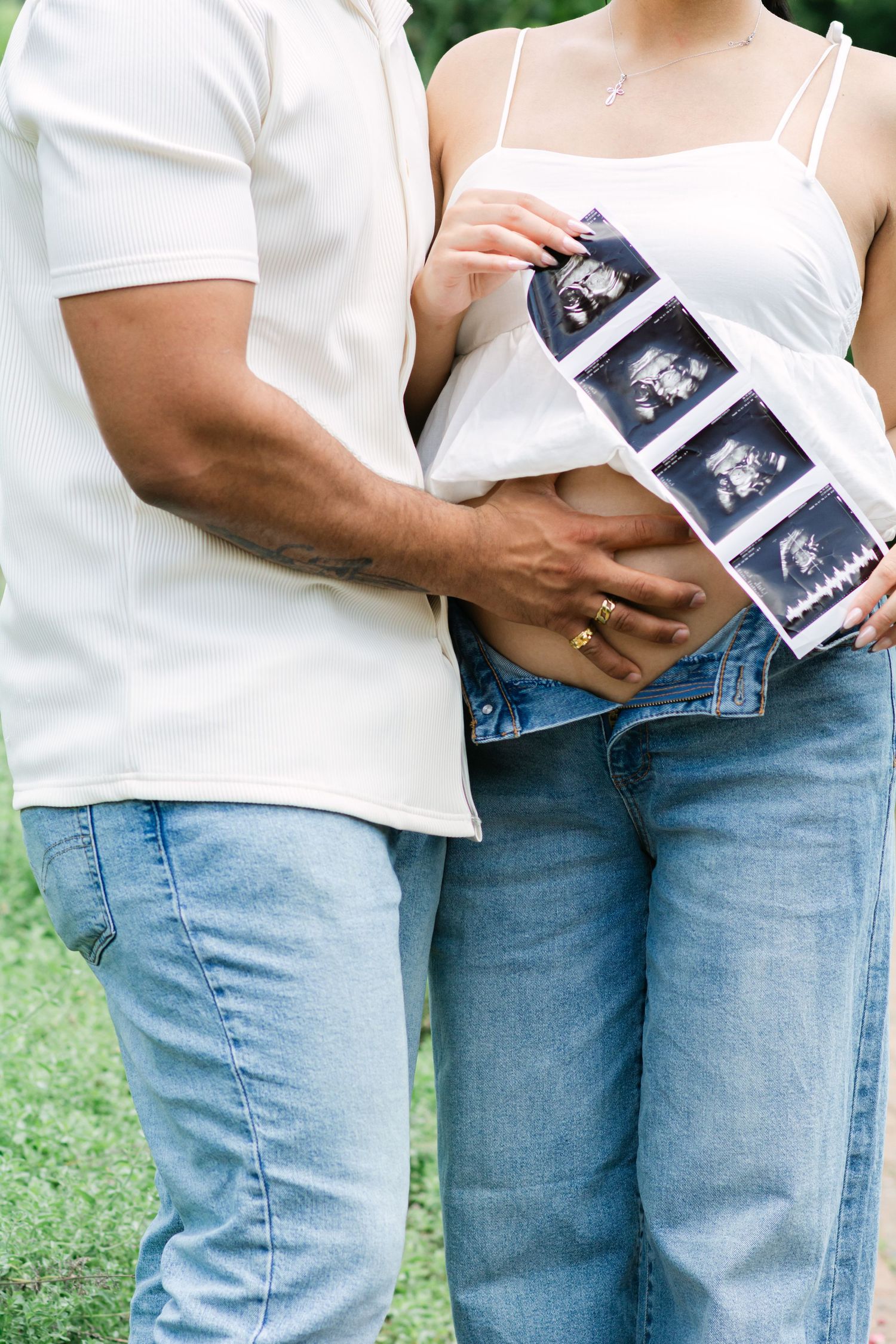 Close-up of a couple in white tops and jeans sharing pregnancy ultrasound images outdoors.