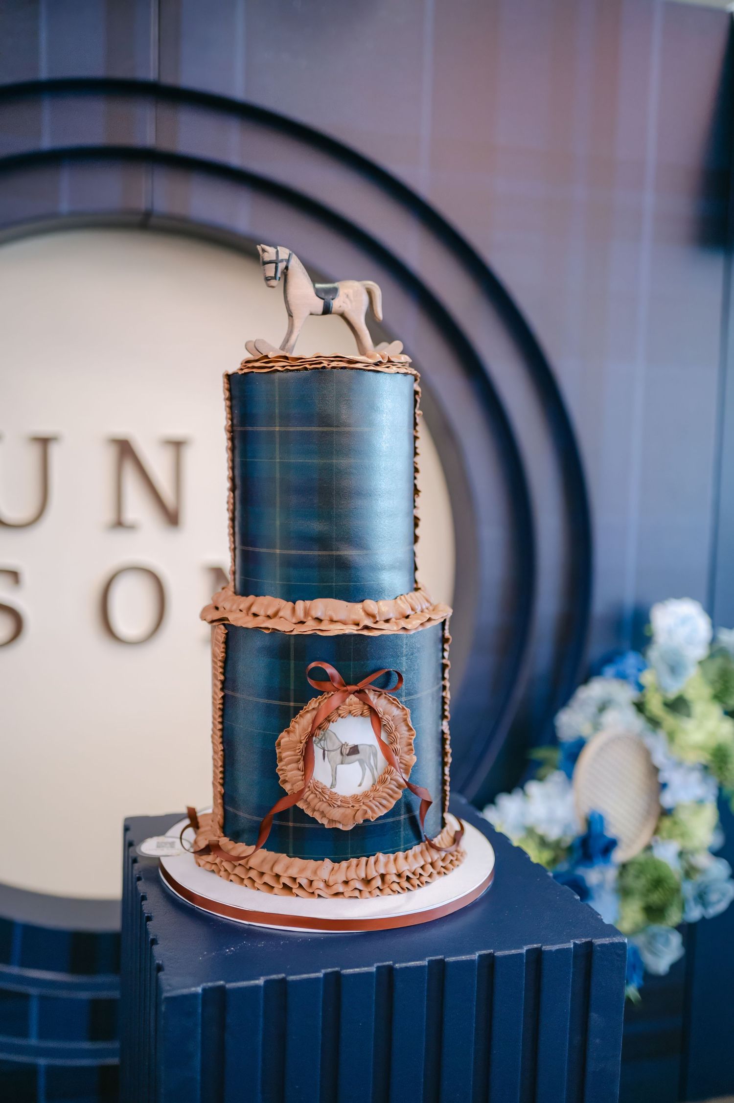 A navy blue and rose gold wedding cake with geometric patterns displayed on a dark surface with floral decor.