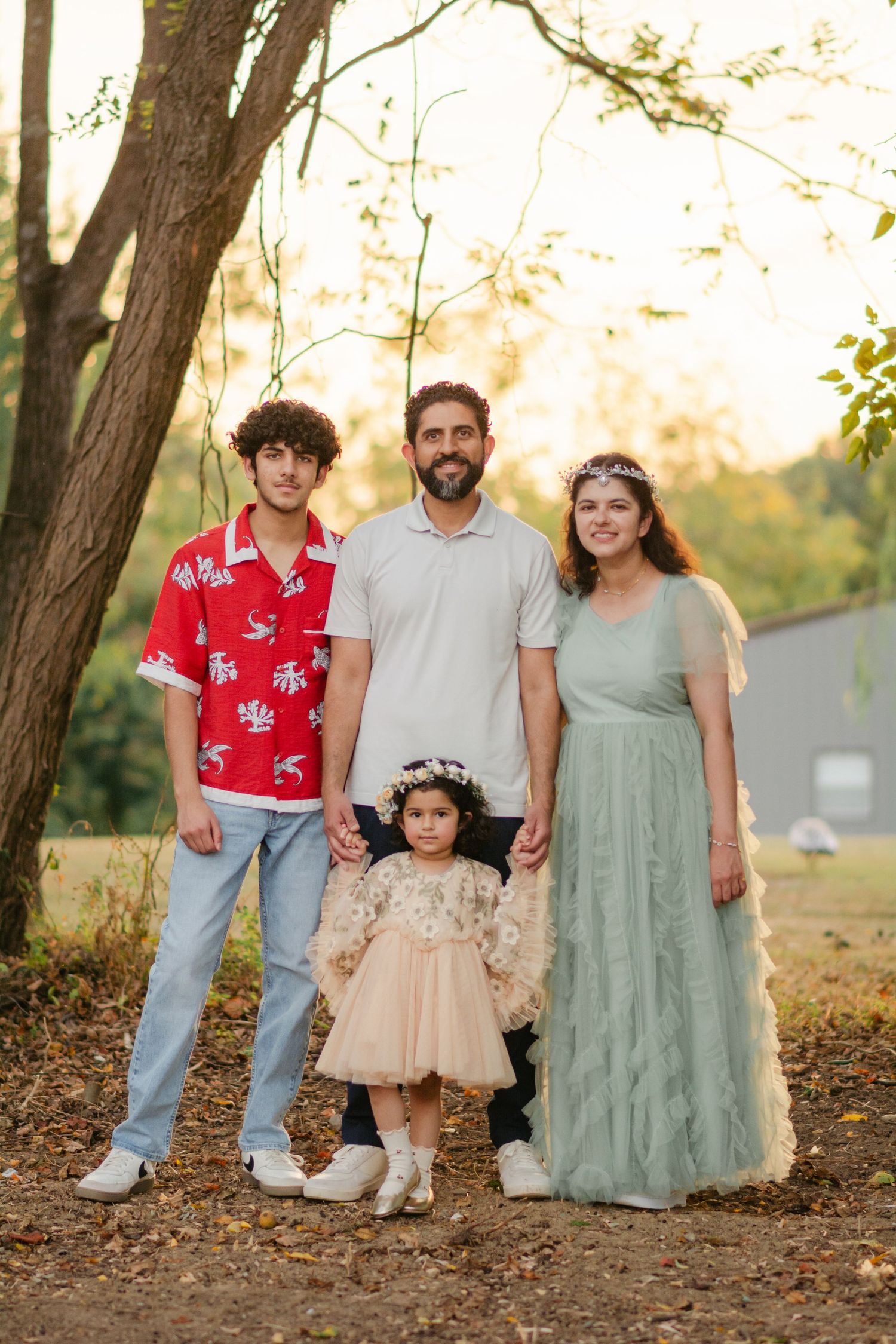 Family portrait session outdoors with autumn trees in the background during golden hour.
