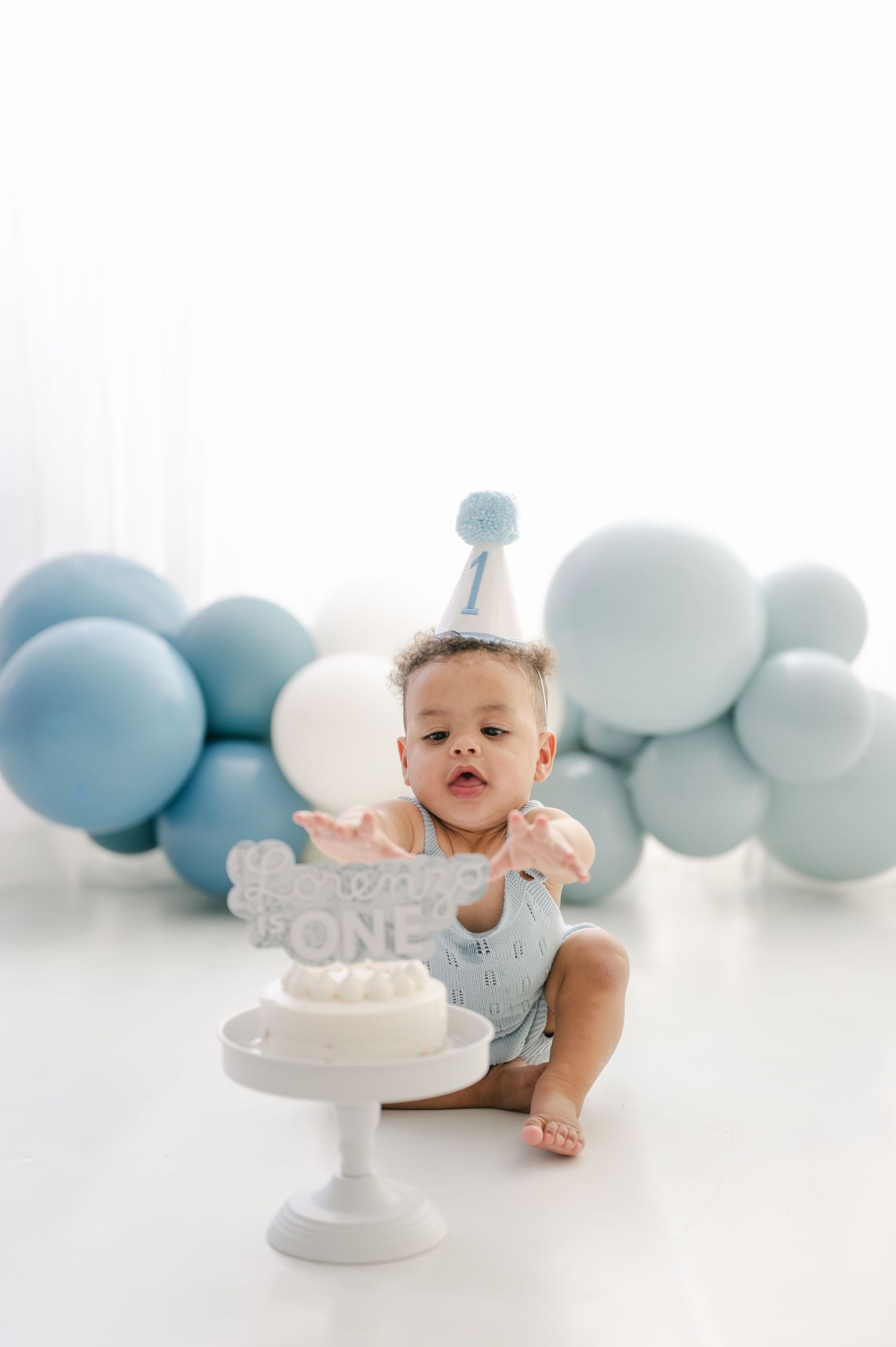 Baby's first birthday cake smash with blue balloons, party hat, and white cake with \
