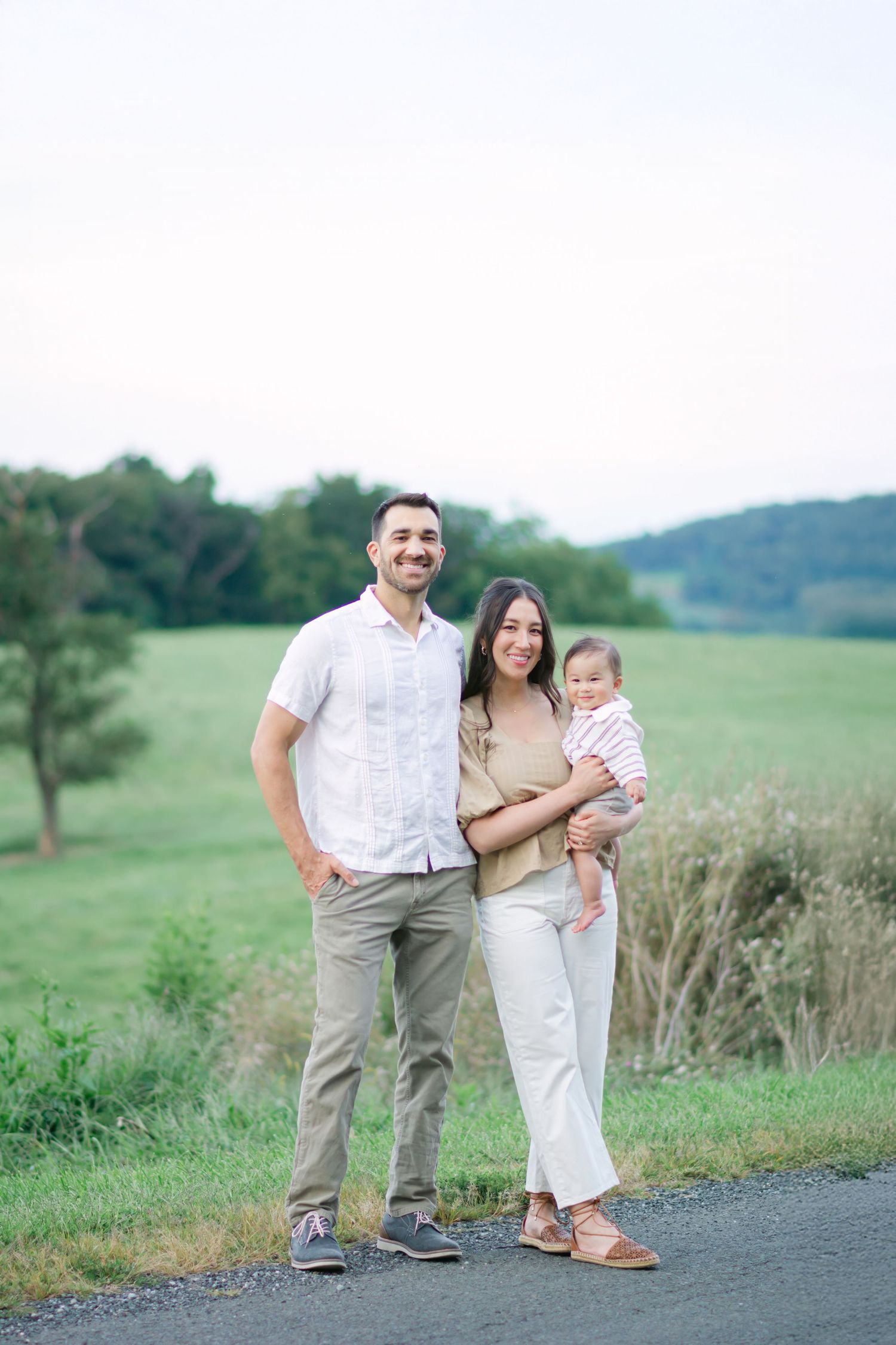 Family members standing together on a gravel path with green countryside hills in the background.