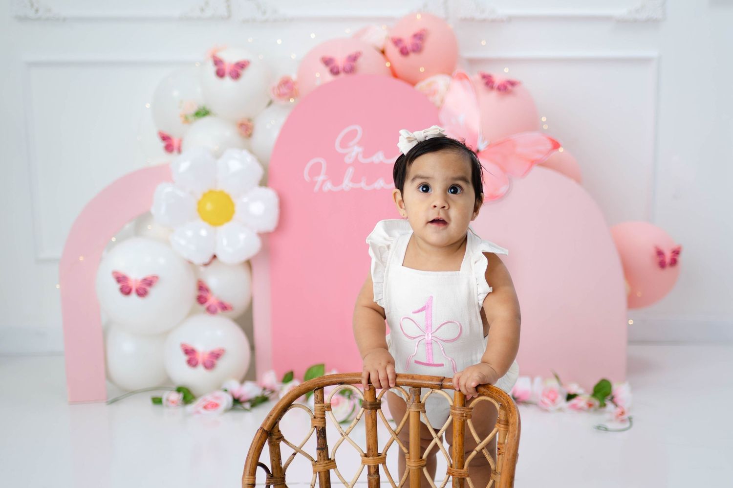 A pink and white themed first birthday party setup with butterflies, flowers, and decorative elements.